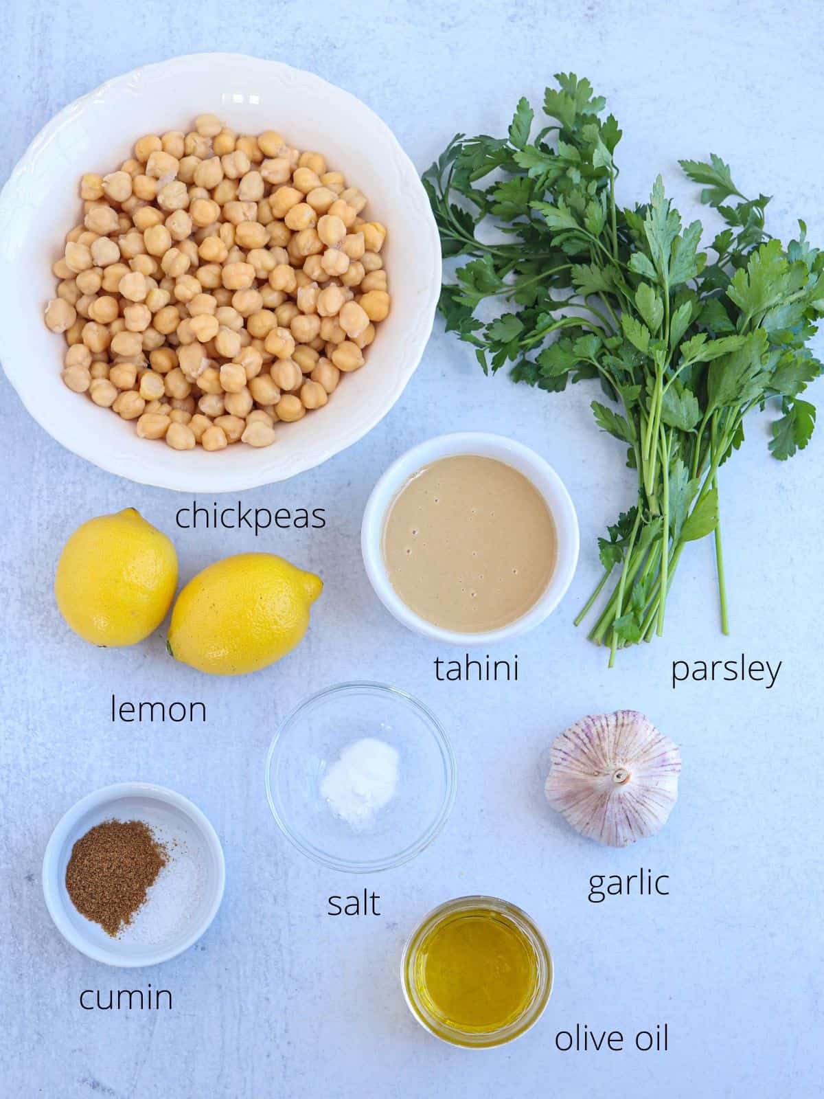 whole chickpea hummus ingredients laid out in bowls on light gray surface with captions.