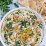 whole chickpea hummus garnished with garlic oil and parsley in a white bowl