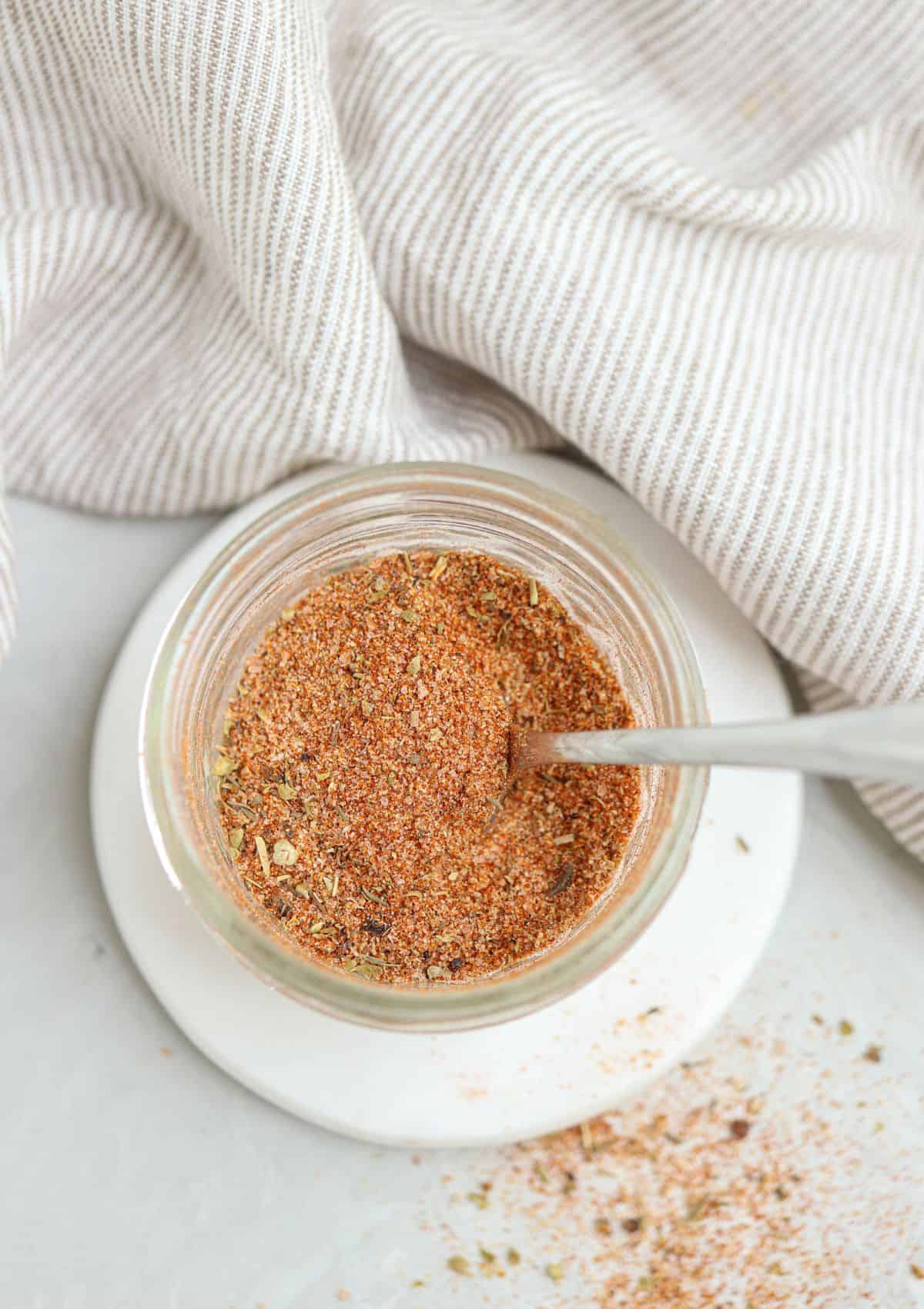 homemade cajun seasoning in a small jar with a spoon inside.