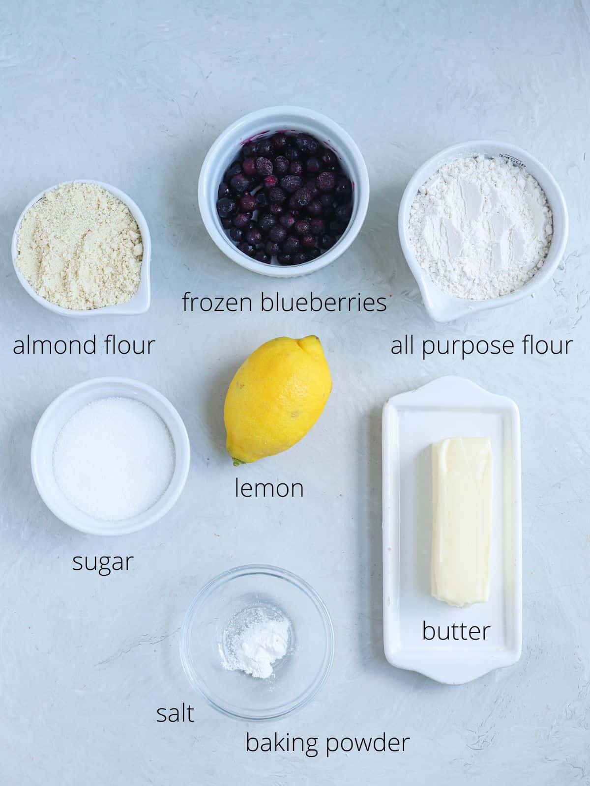 ingredients for blueberry lemon cookies on light gray surface with captions.