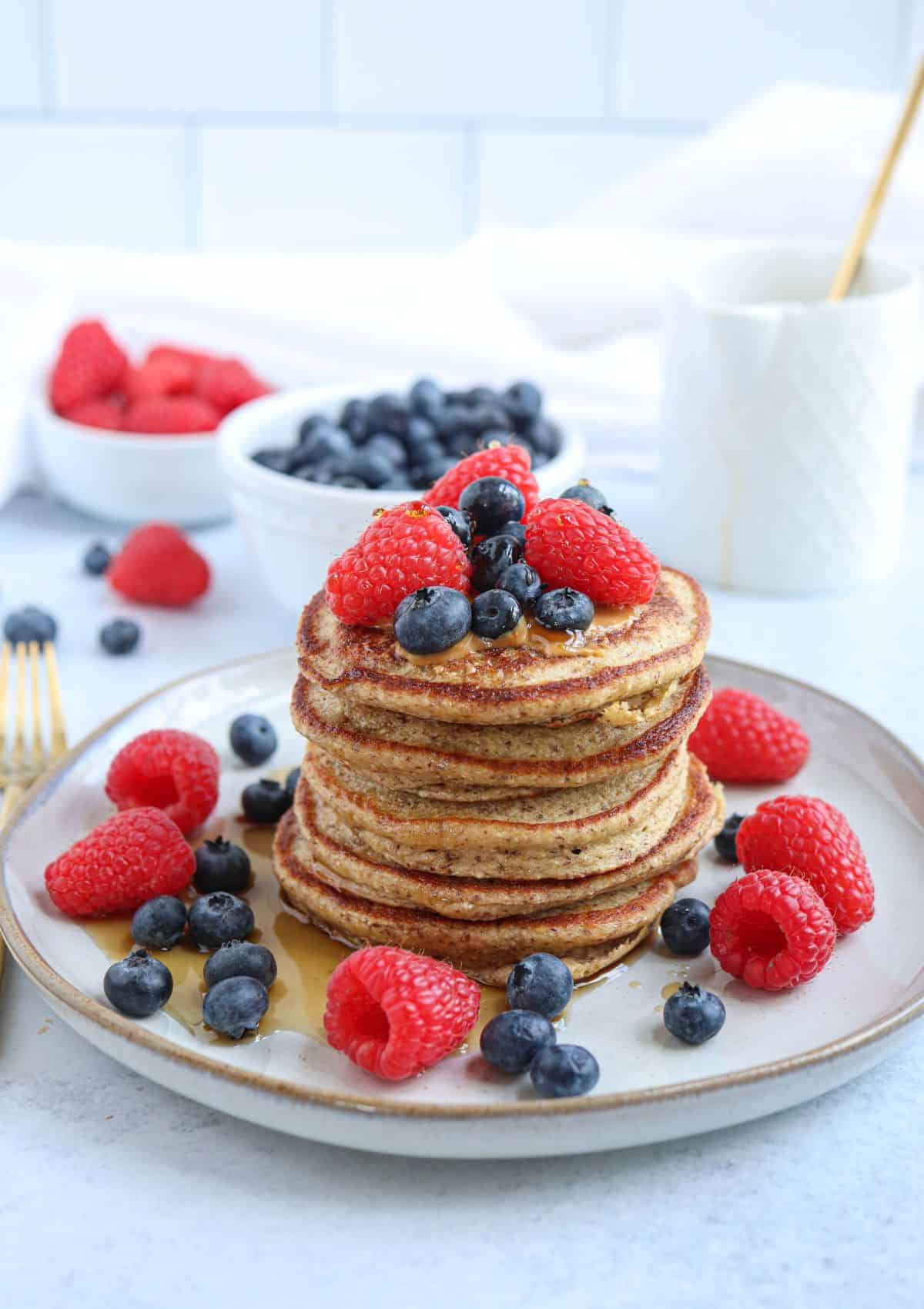 a stack of five protein banana oatmeal pancakes topped with fresh berries and  maple syrup on a gray plate.