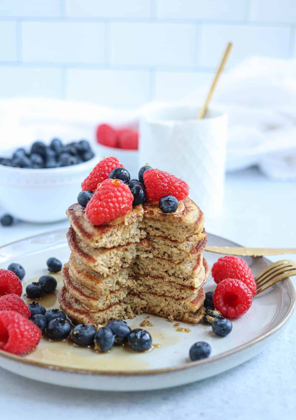 a stack of five protein banana oatmeal pancakes topped with fresh berries and  maple syrup on a gray plate with a big triangular piece cut out.