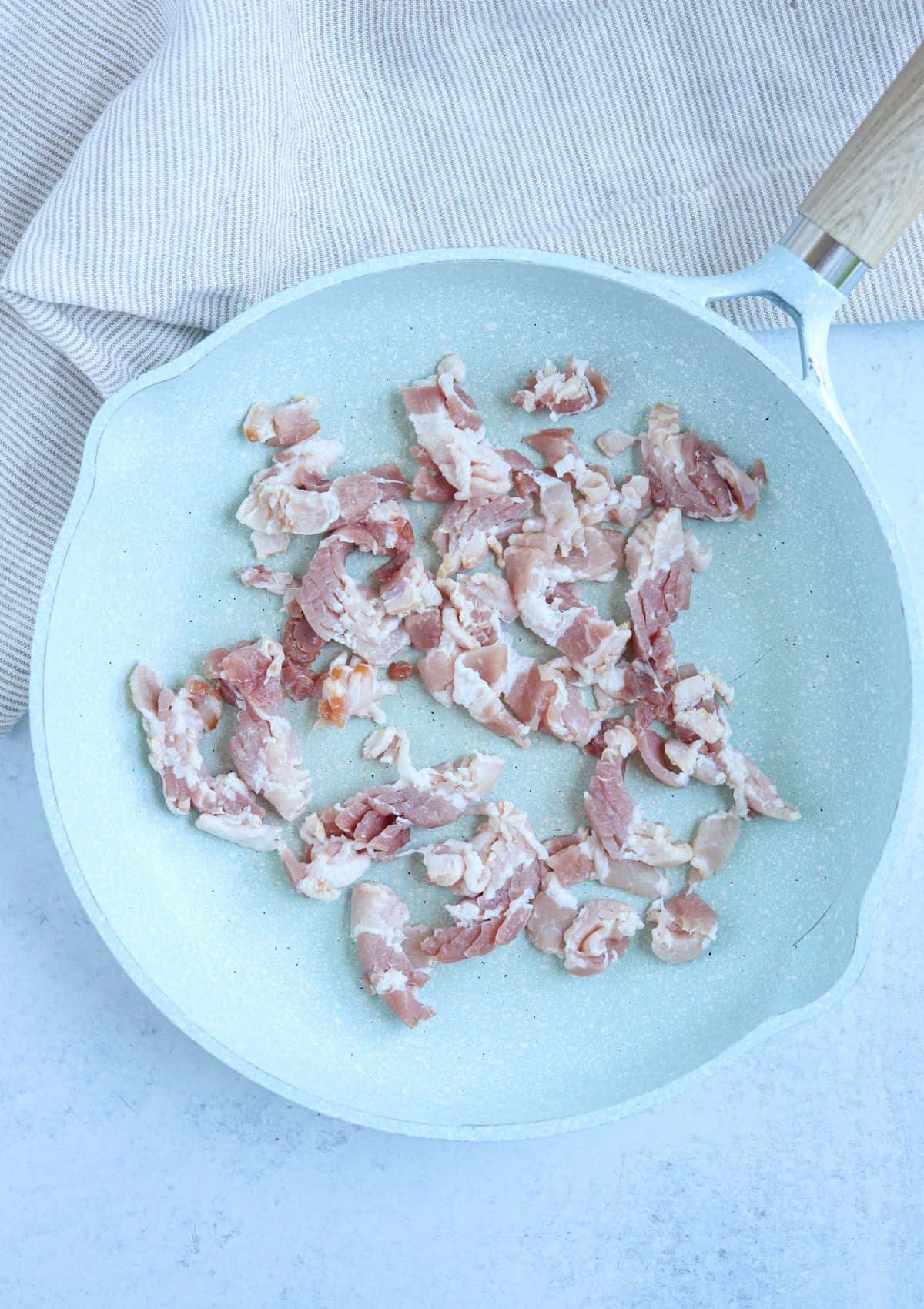 raw bacon bits before cooking in a light blue skillet.