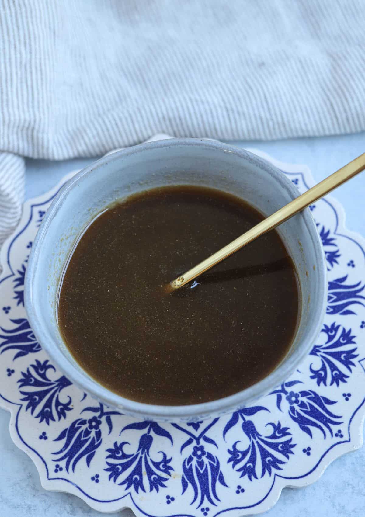 sauce made with soy sauce, maple syrup and melted butter in a small gray bowl with a golden spoon.