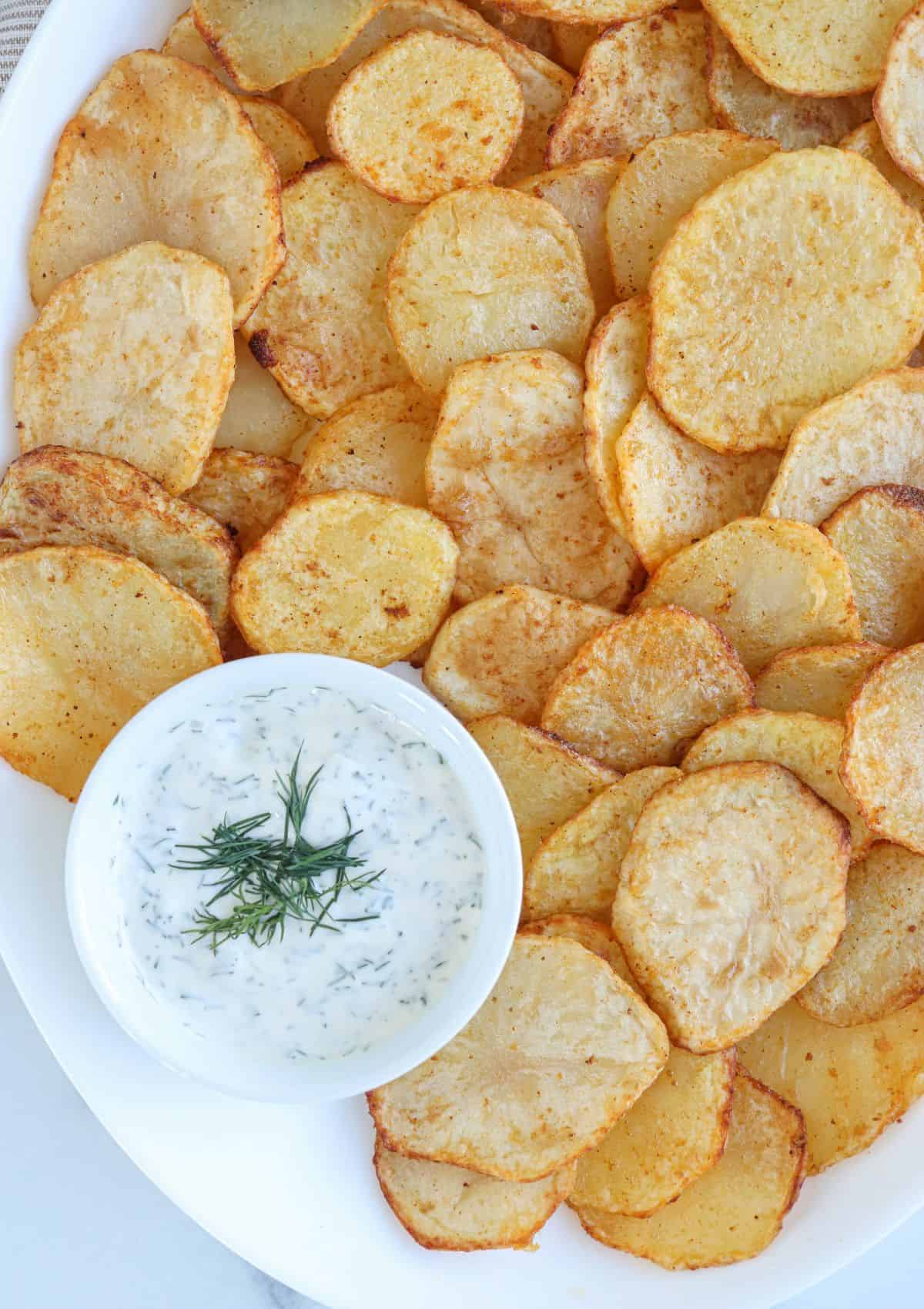 sliced air fried potatoes on a white platter with a side of dill aioli.