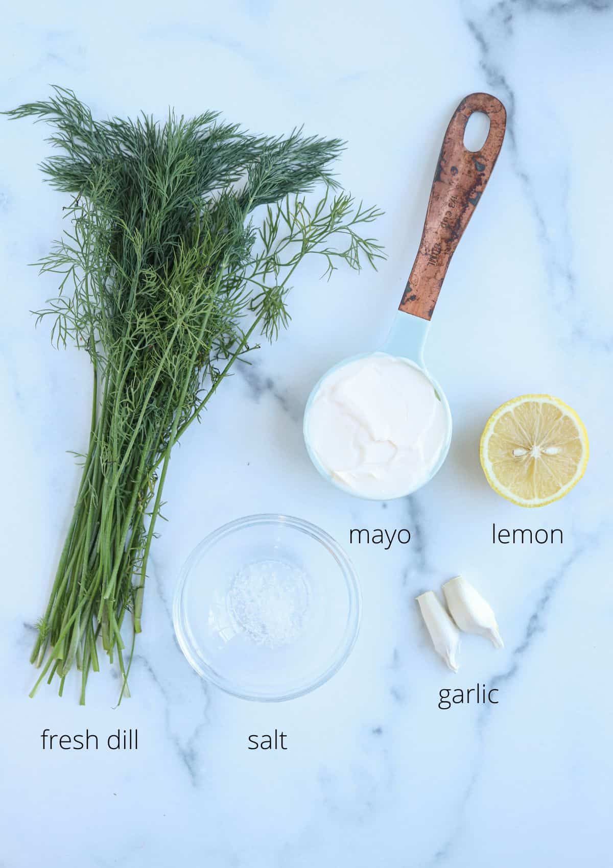 ingredients for making dill aioli on a white marble surface with captions. 