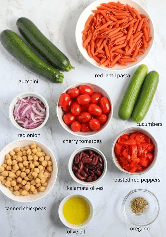 ingredients for a red lentil pasta salad on white marble surface with captions.