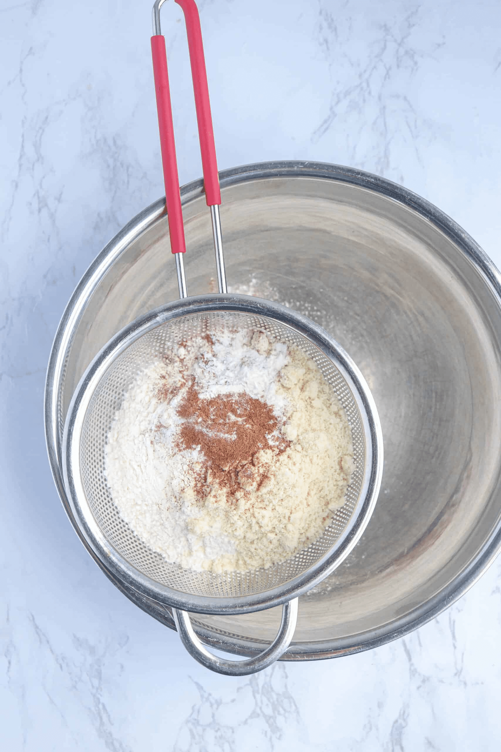 a sieve with flour, almond flour and cinnamon over a steel bowl.