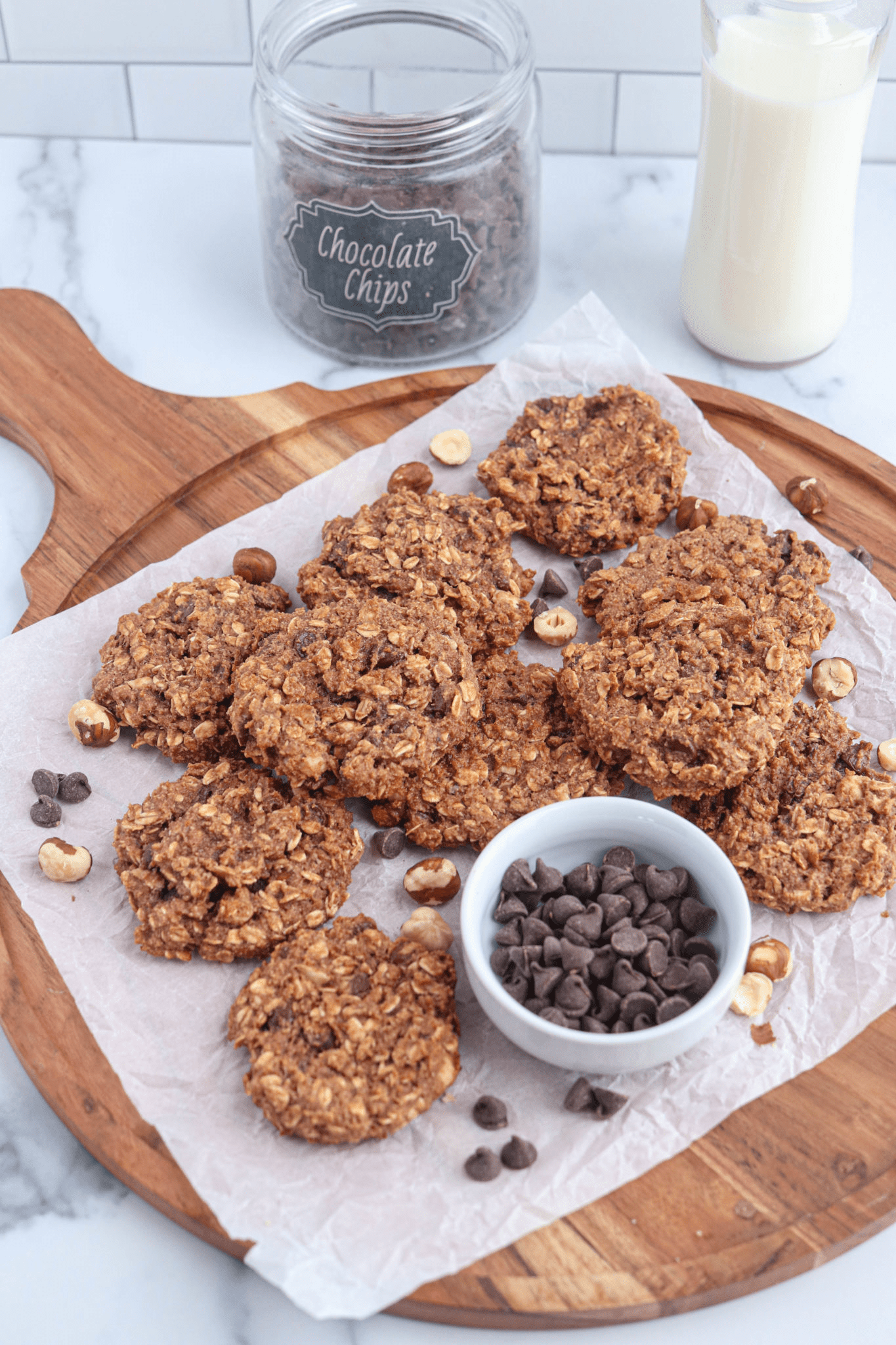 banana nutella oatmeal cookies on paper lined round wooden board with a small container of chocolate chips. 