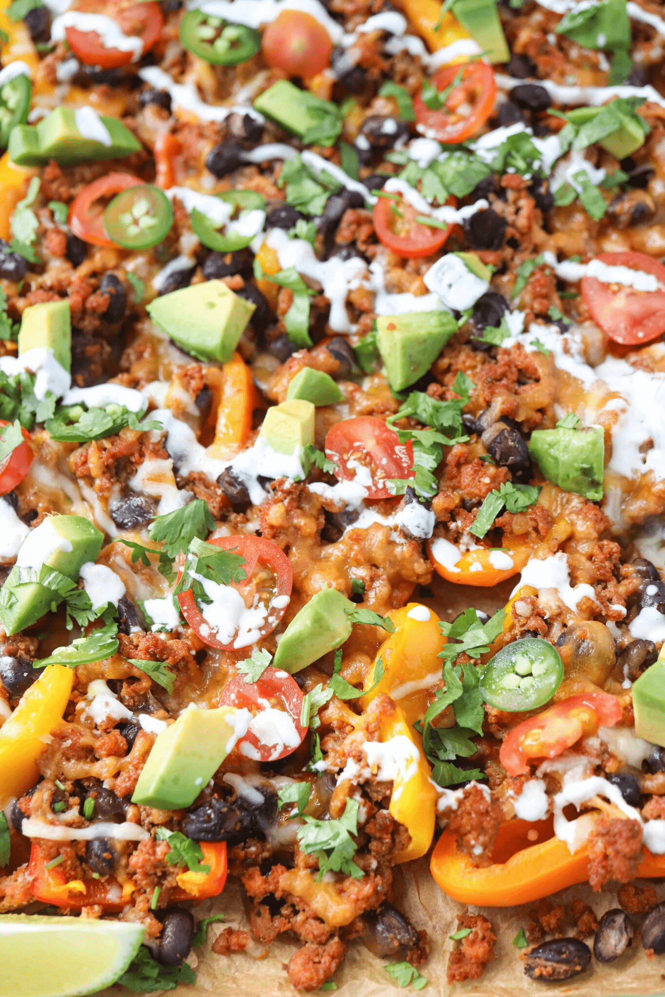 mini pepper nachos with ground meat, avocado and garnishes on teal baking tray.