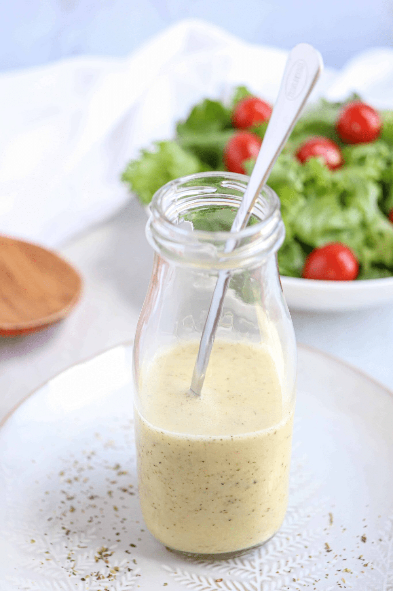 Greek salad dressing in a glass bottle with a spoon inside on a gray plate.