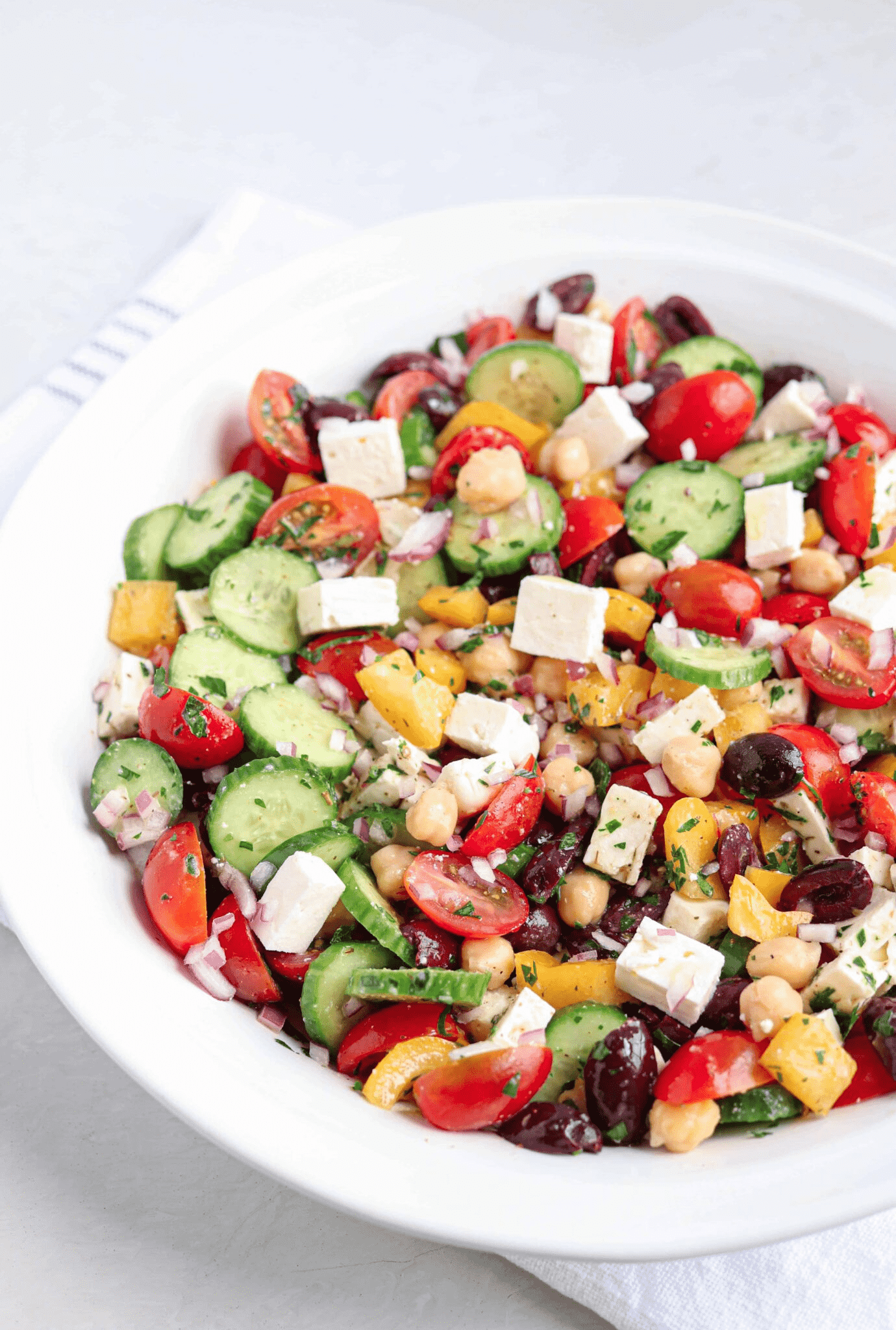 Greek chickpea salad with feta cheese, tomatoes, cucumbers and chickpeas in a large white bowl.