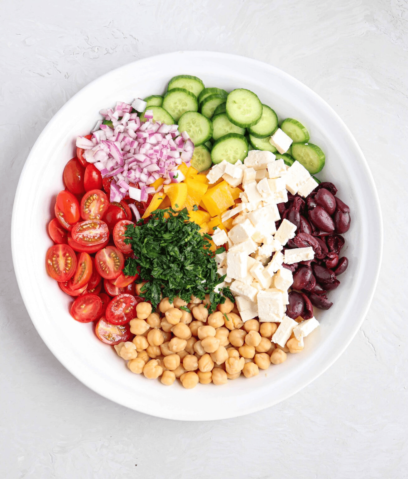 Greek chickpea salad with feta cheese, tomatoes, cucumbers and chickpeas in a large white bowl, before mixing.