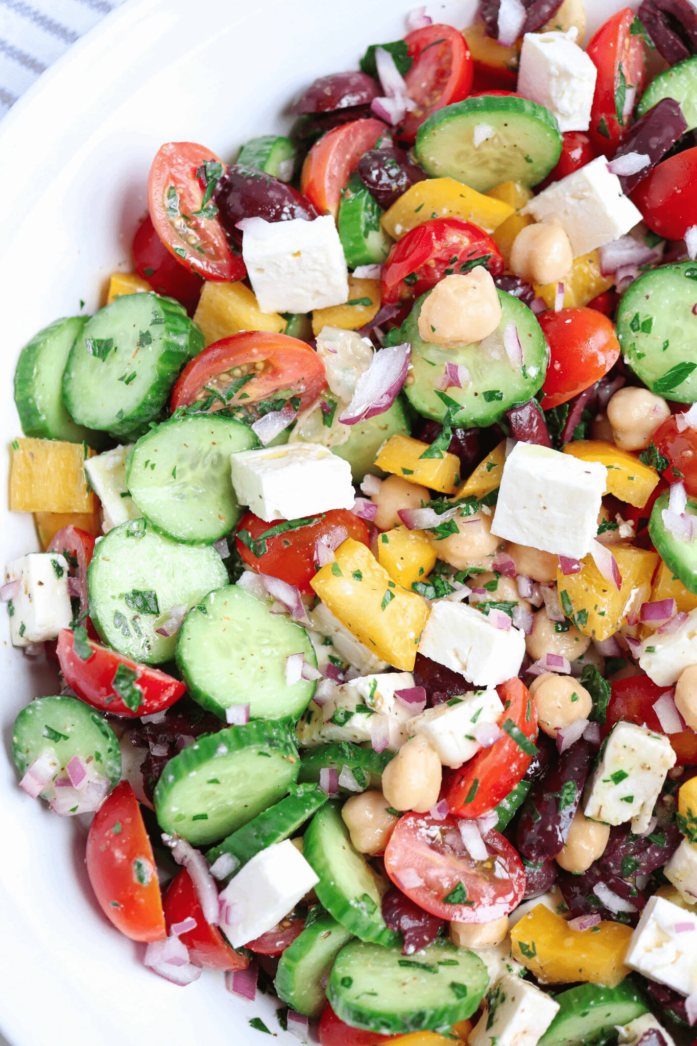 Greek chickpea salad with feta cheese, tomatoes, cucumbers and chickpeas in a large white bowl.