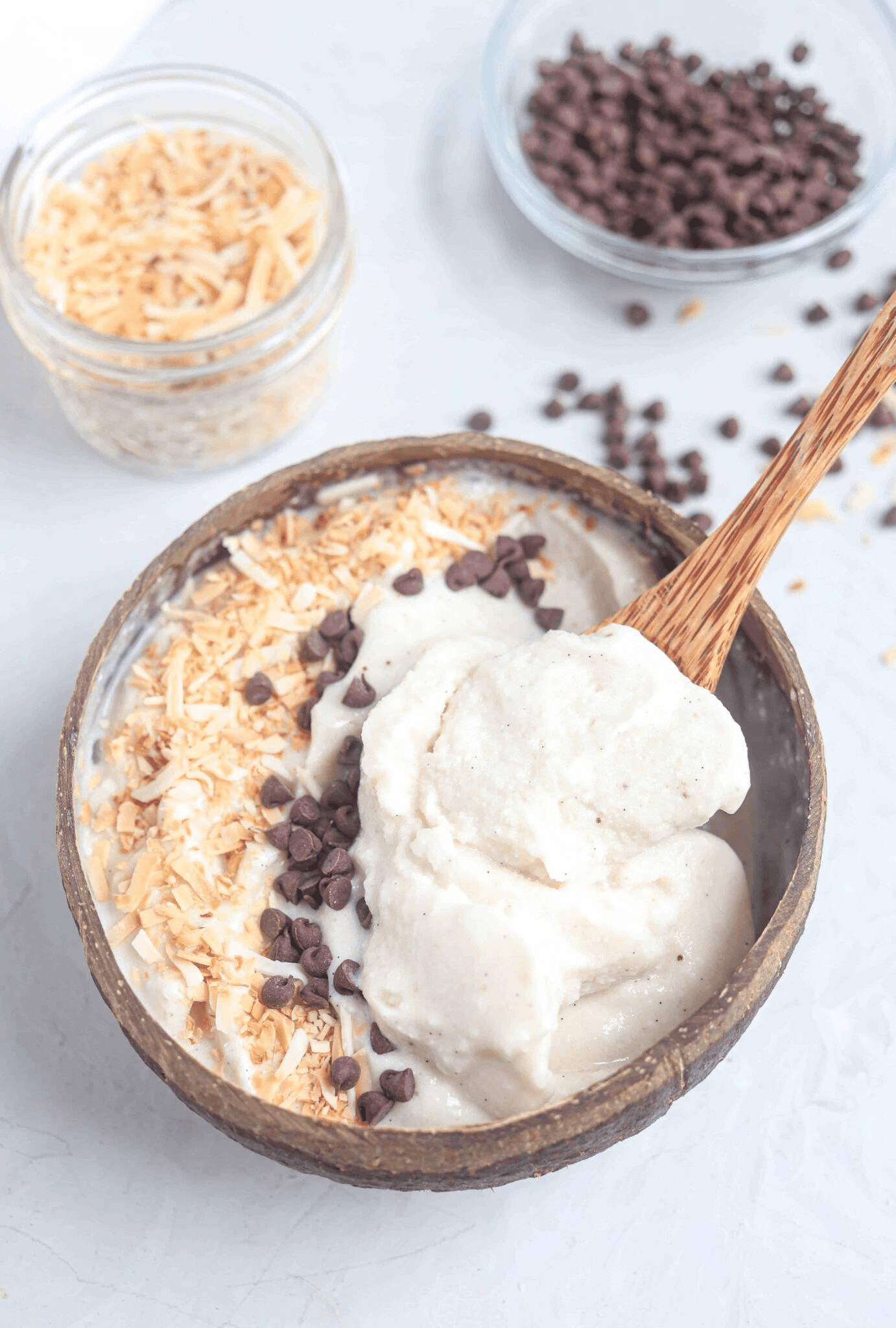 coconut vanilla smoothie bowl topped with toasted coconut and mini chocolate chips in a natural coconut shell, bite shot.