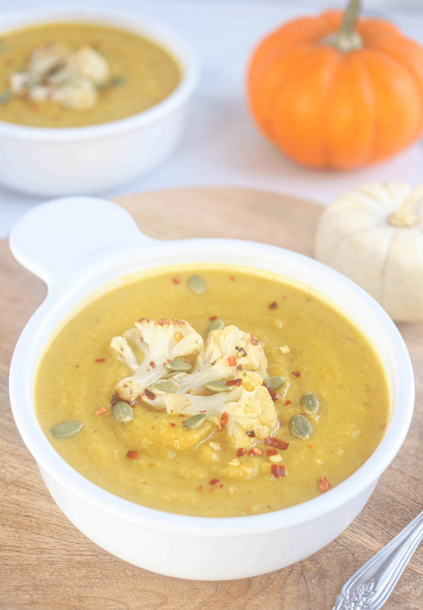 pumpkin cauliflower soup in a white bowl topped with cauliflower, pepitas and pepper flakes. 