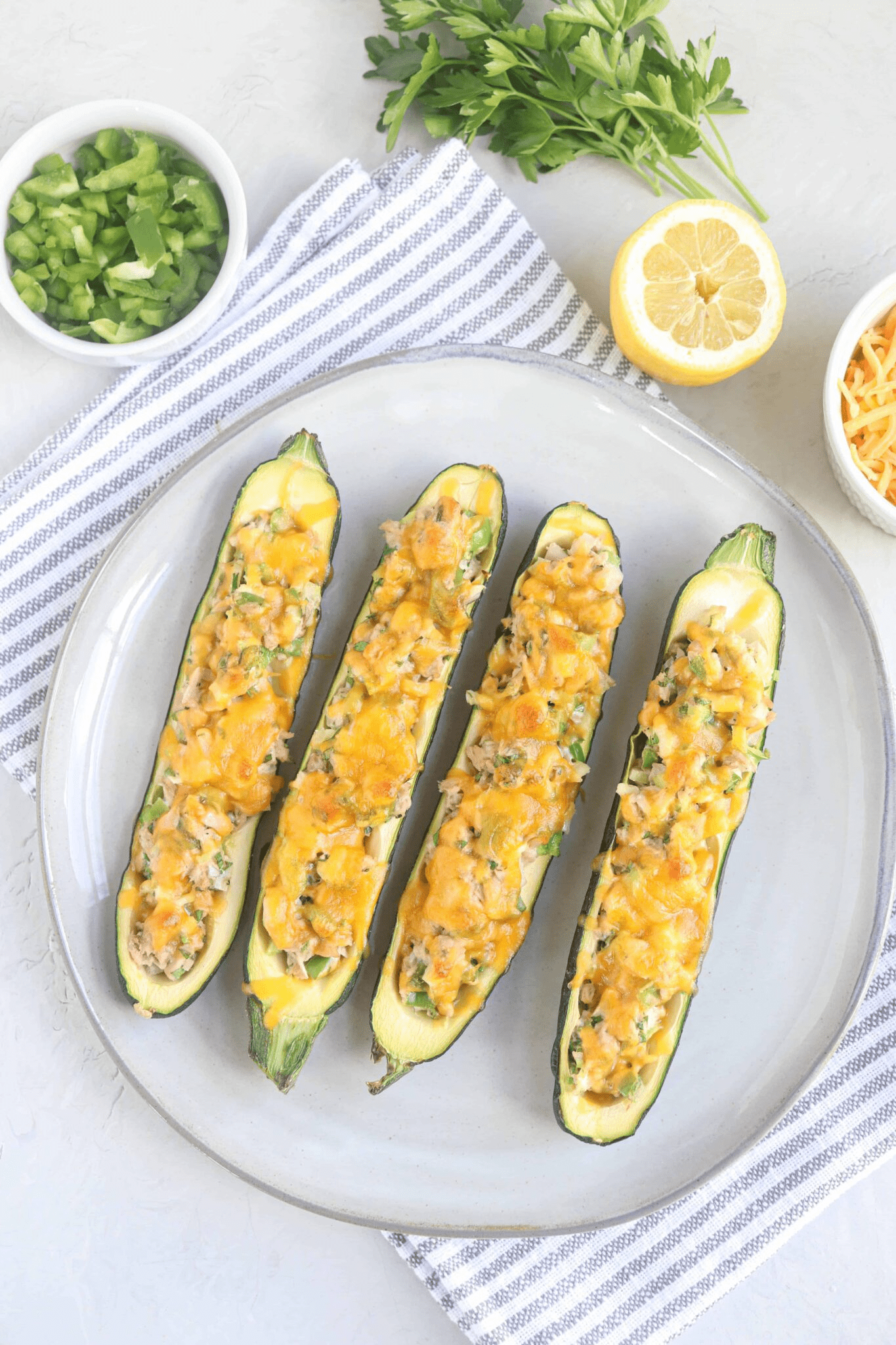 four zucchini boats filled with tuna salad and melted cheese on a gray plate. 