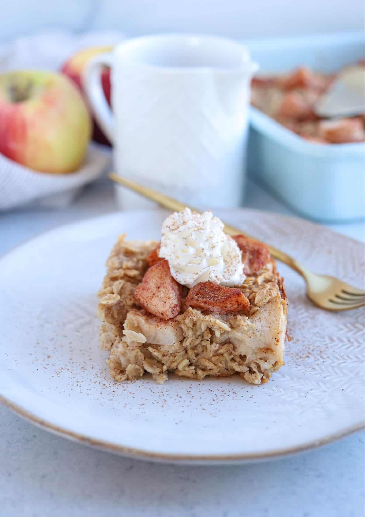 apple pie baked oatmeal square topped with cooked apples, whipped cream, cinnamon and maple syrup.