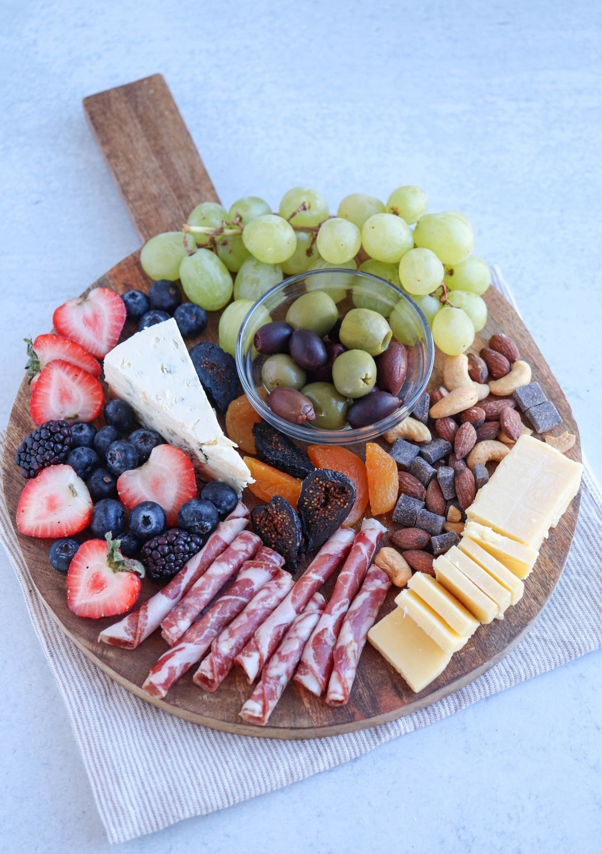 a small round charcuterie board with cheese, grapes, salami, nuts and olives.