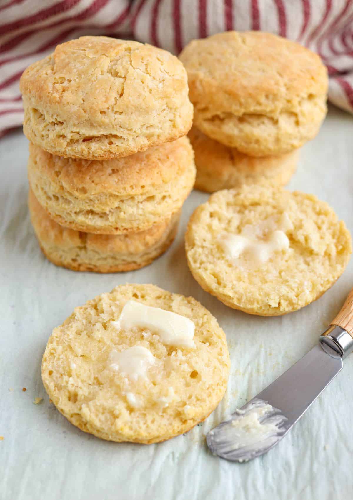 freshly baked round biscuits, stacked on parchment paper, one biscuit split and smeared with butter.