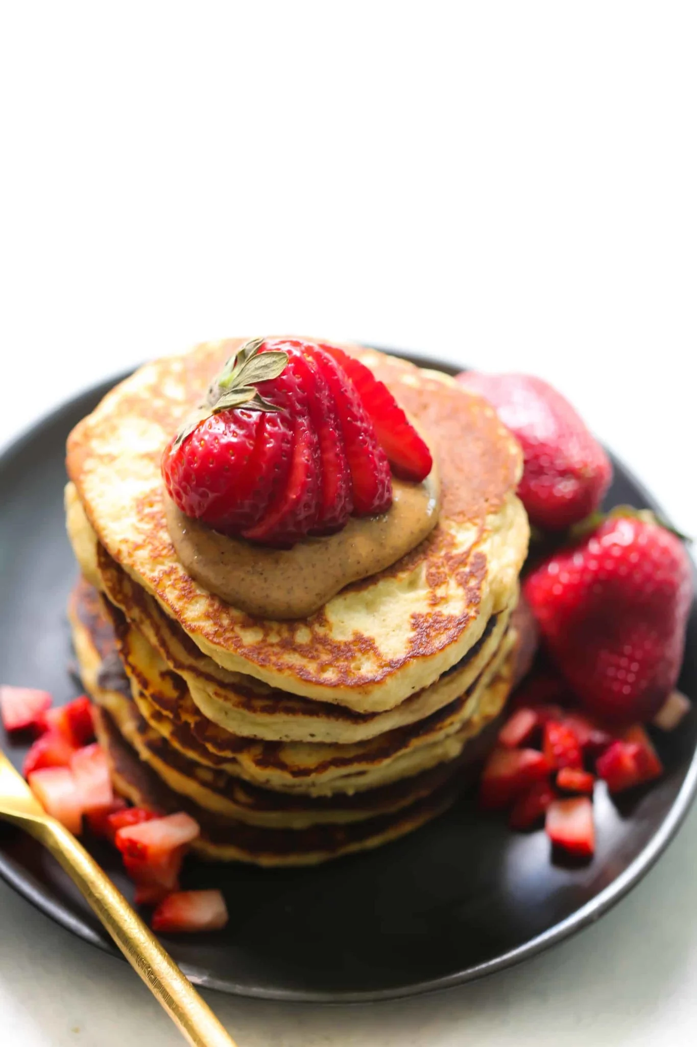 a stack of healthy banana pancakes topped with nut butter and fresh strawberries.