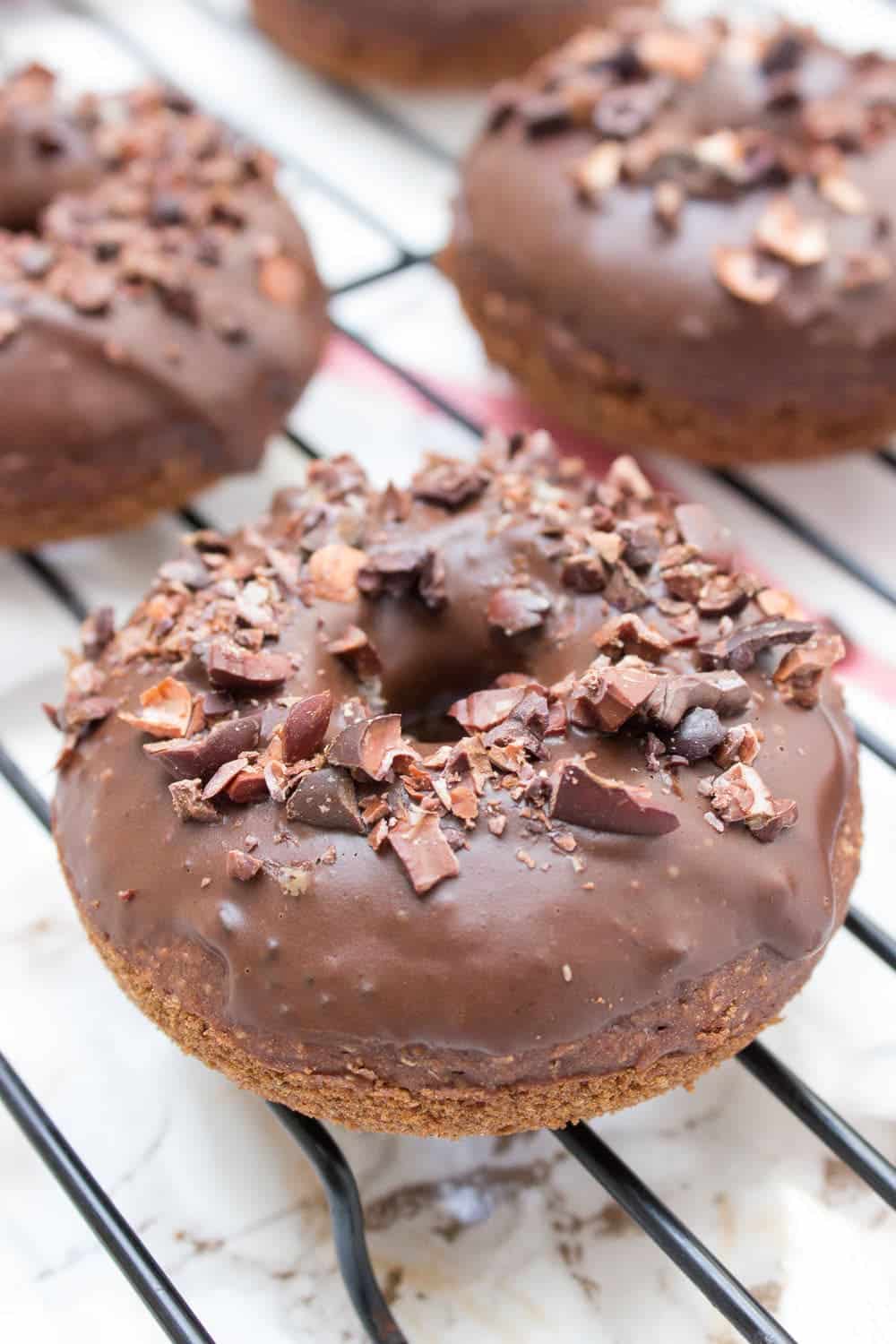 chocolate banana donuts glazed with chocolate and topped with chocolate chunks on a black cooling rack.