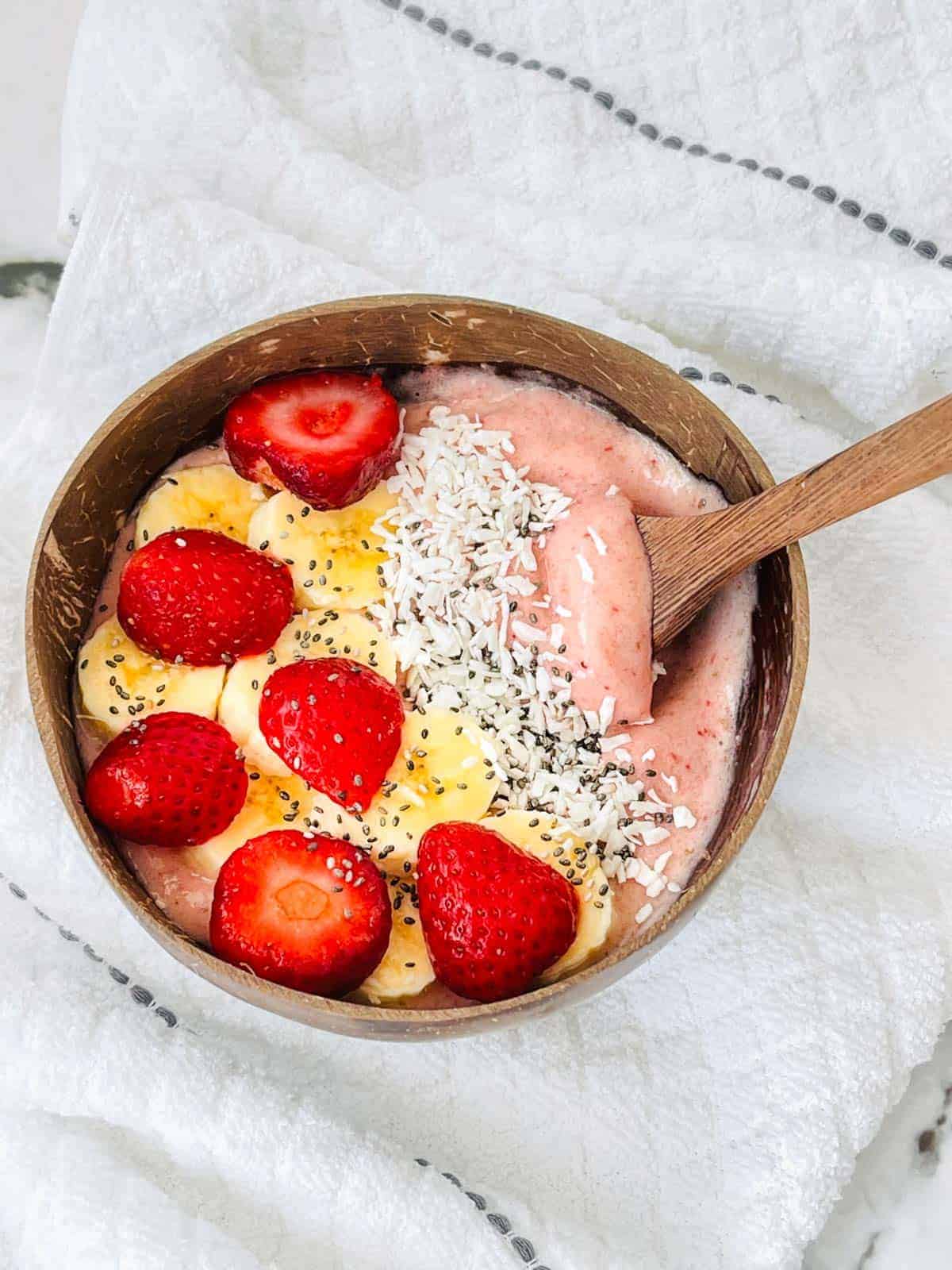 banana strawberry smoothie bowl with fresj fruit toppings, coconut and chia seeds in a coconut bowl.