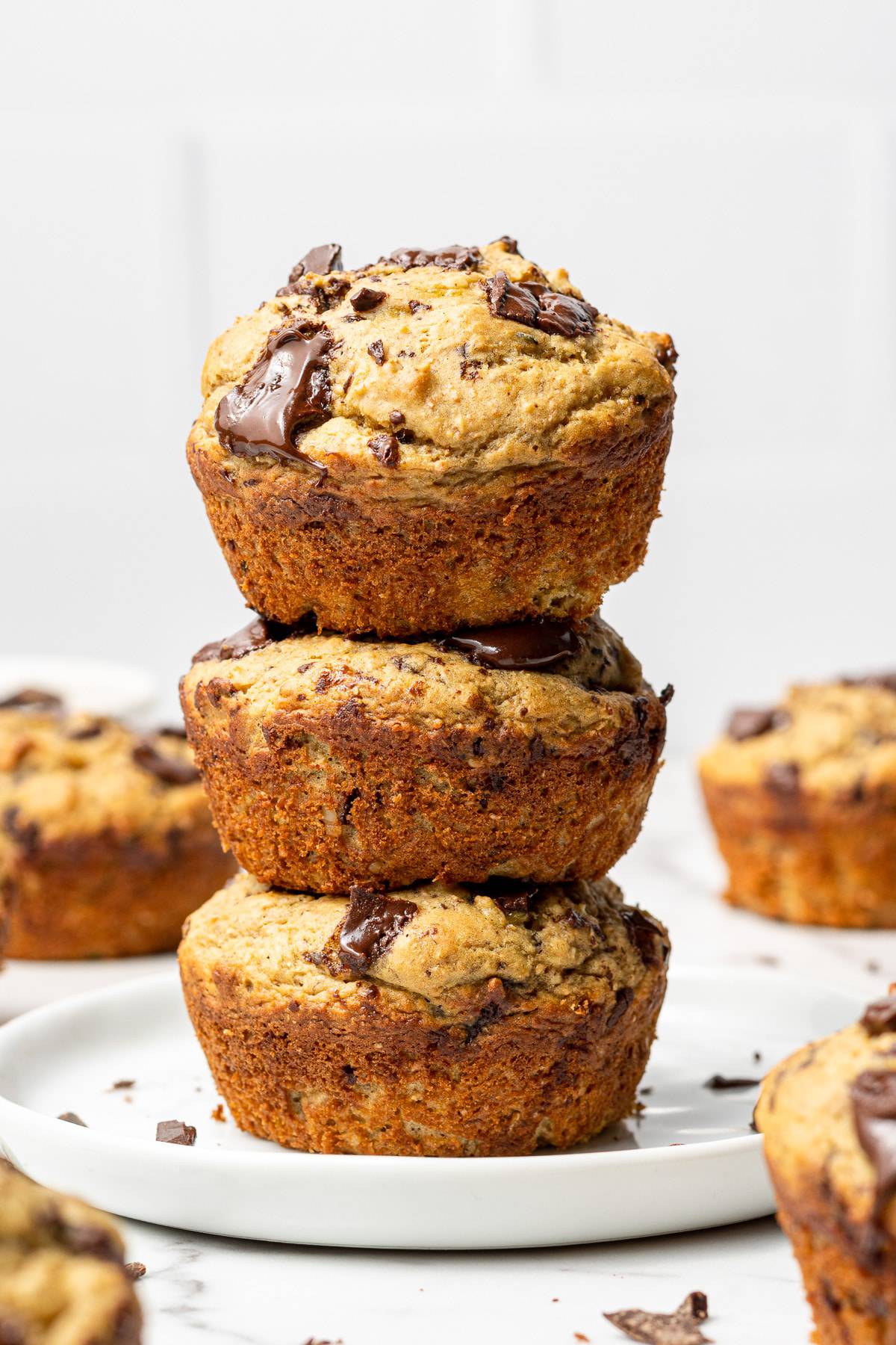 3 banana protein chocolate chip muffins stacked on a white plate.