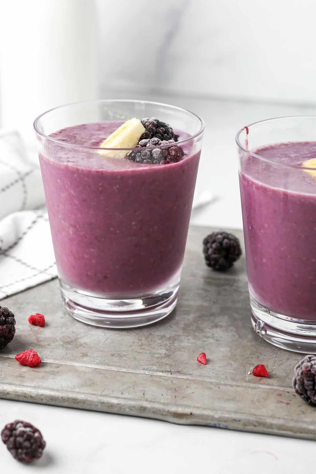 strawberry blackberry banana smoothie in two glassed garnished with banana and blackberries.