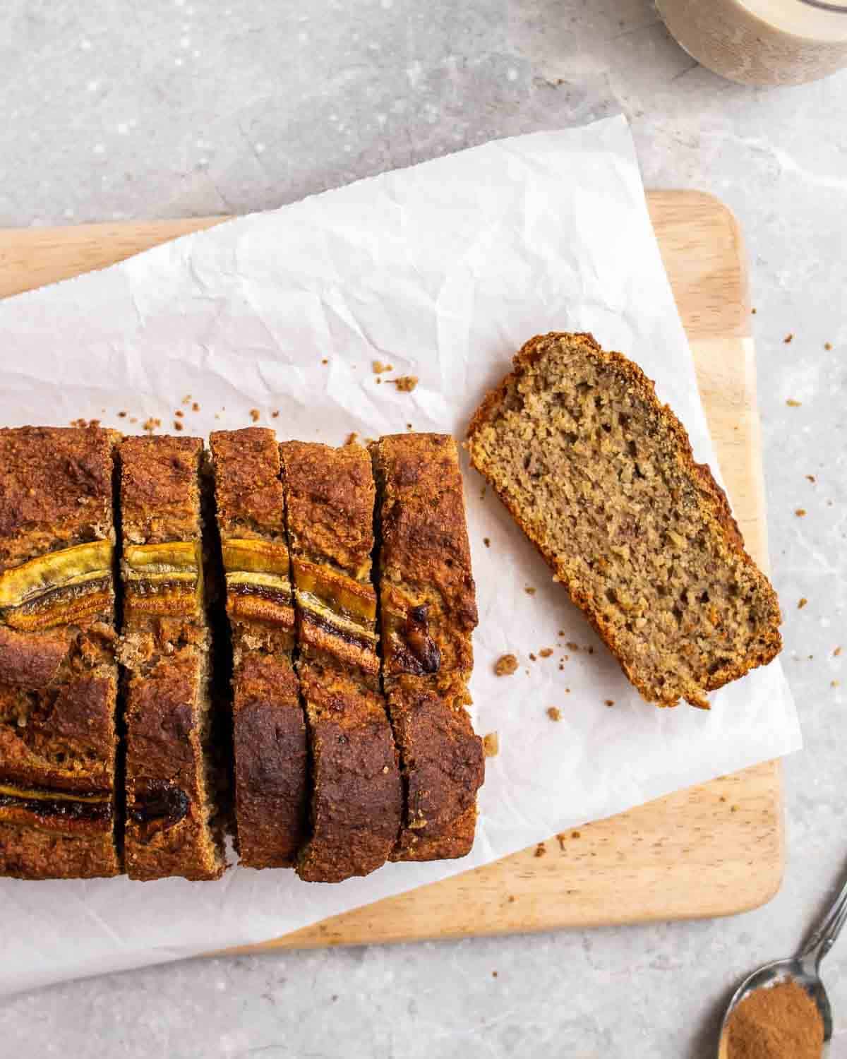 banana bread loaf sliced on paper on a wooden board.