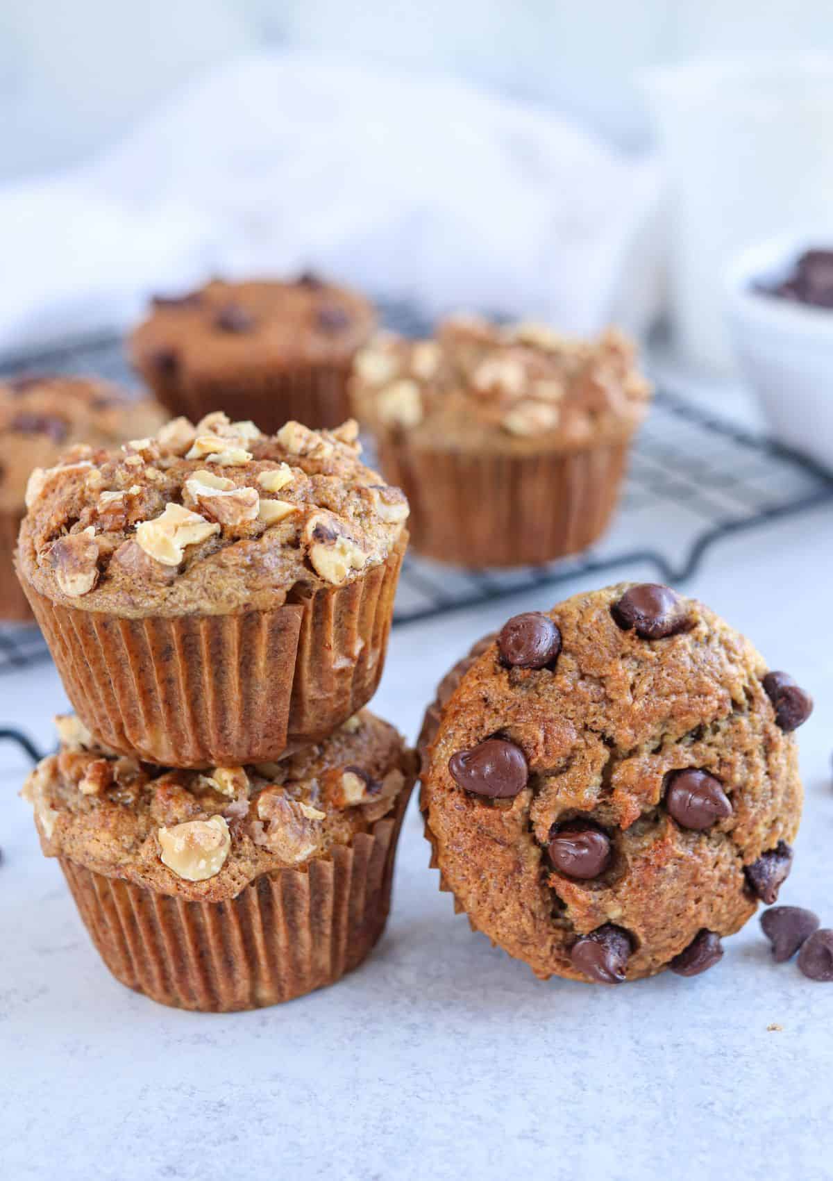 banana muffins with walnuts and chocolate chips stacked on light gray surface.