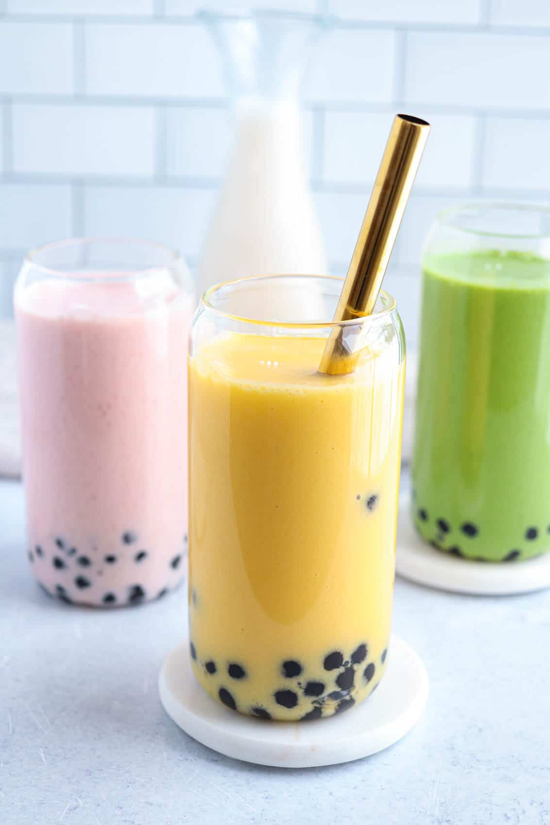 three boba smoothies: yellow, pink and green in beer can shaped glasses.