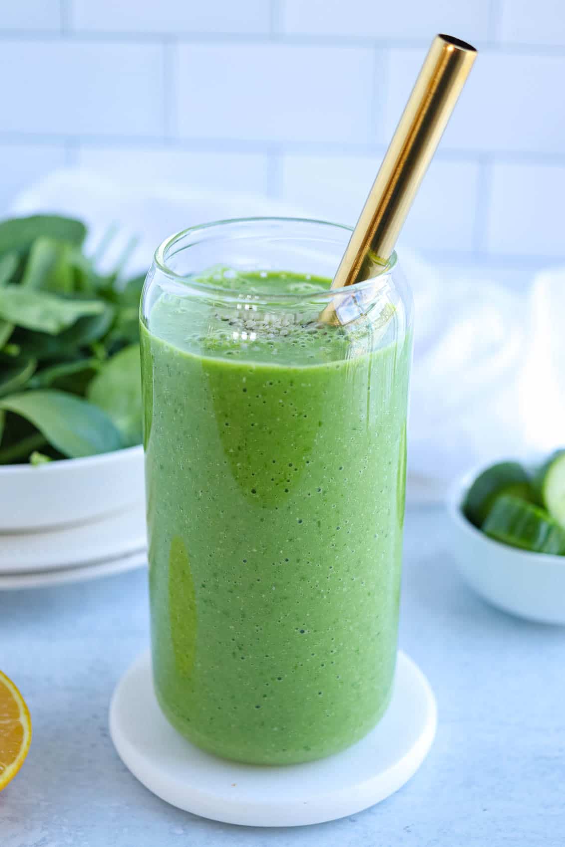 green spinach smoothie in a tall glass with a golden straw.