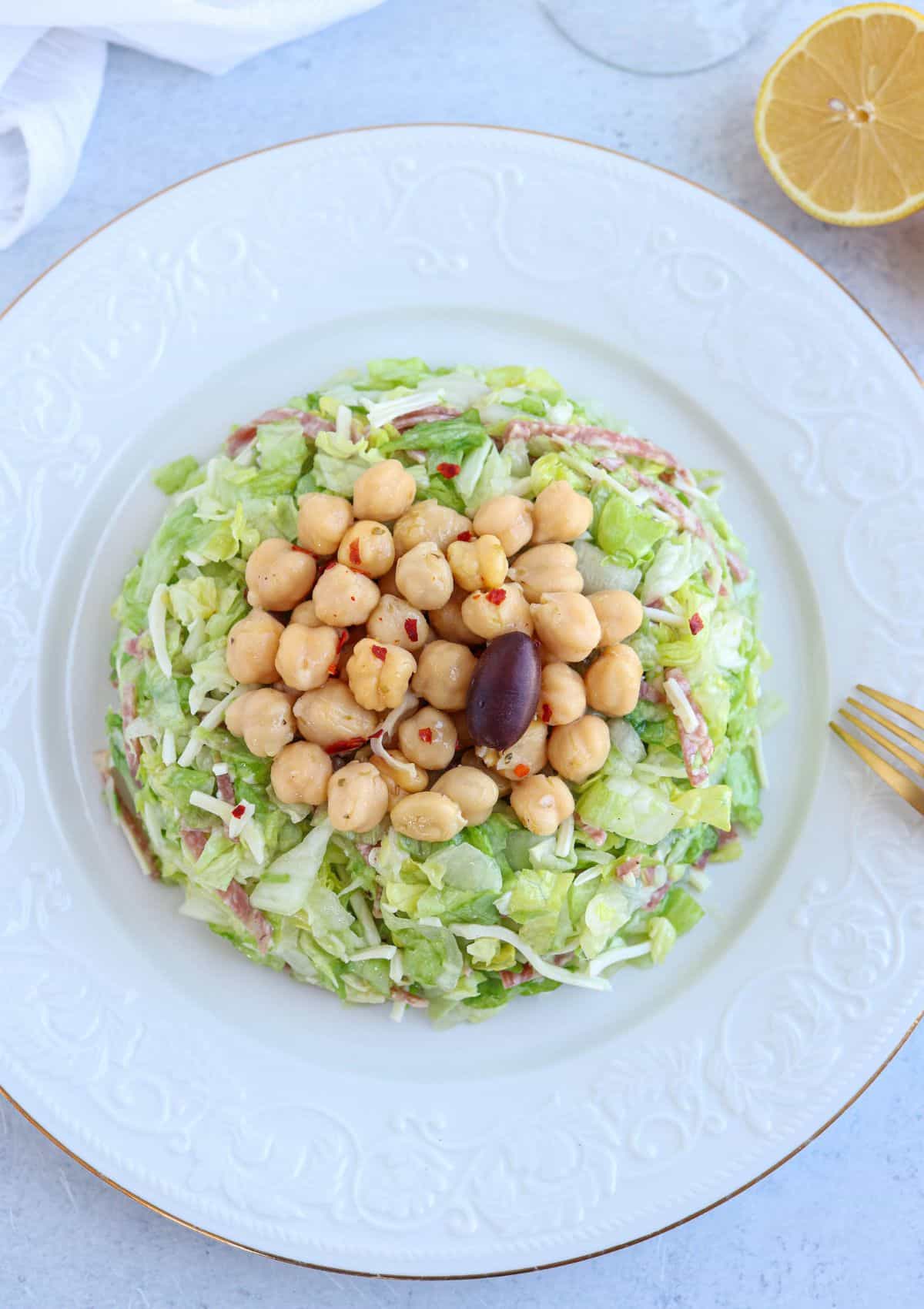 chopped salad with salami, mozzarella and marinated chickpeas on top on a white plate, overhead view.