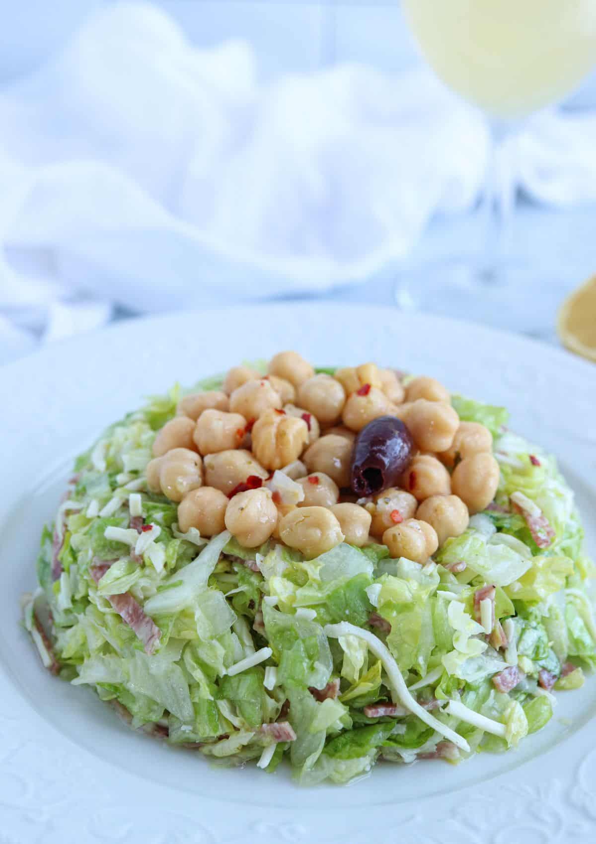 chopped salad with salami, mozzarella and marinated chickpeas on top on a white plate.