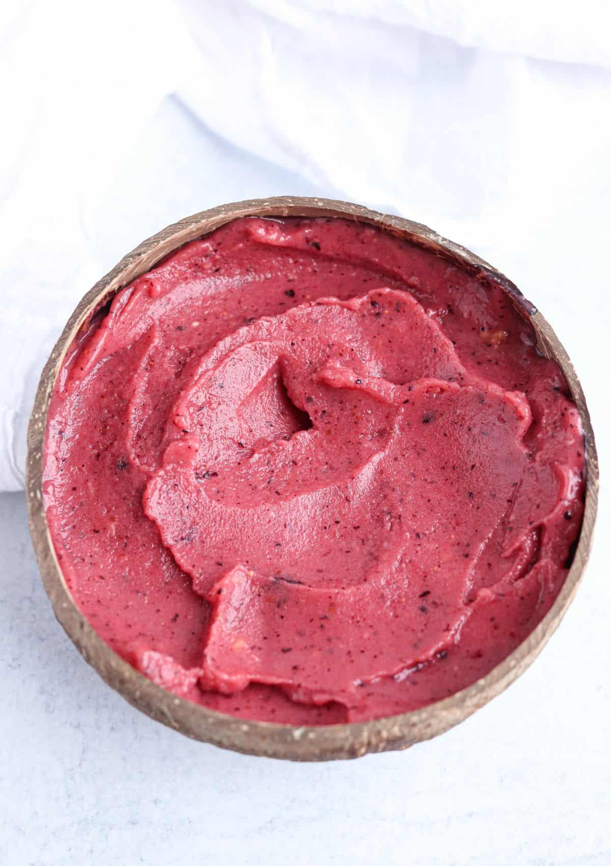 thick smoothie bowl made with frozen berries and mangoes in a coconut shell bowl. 