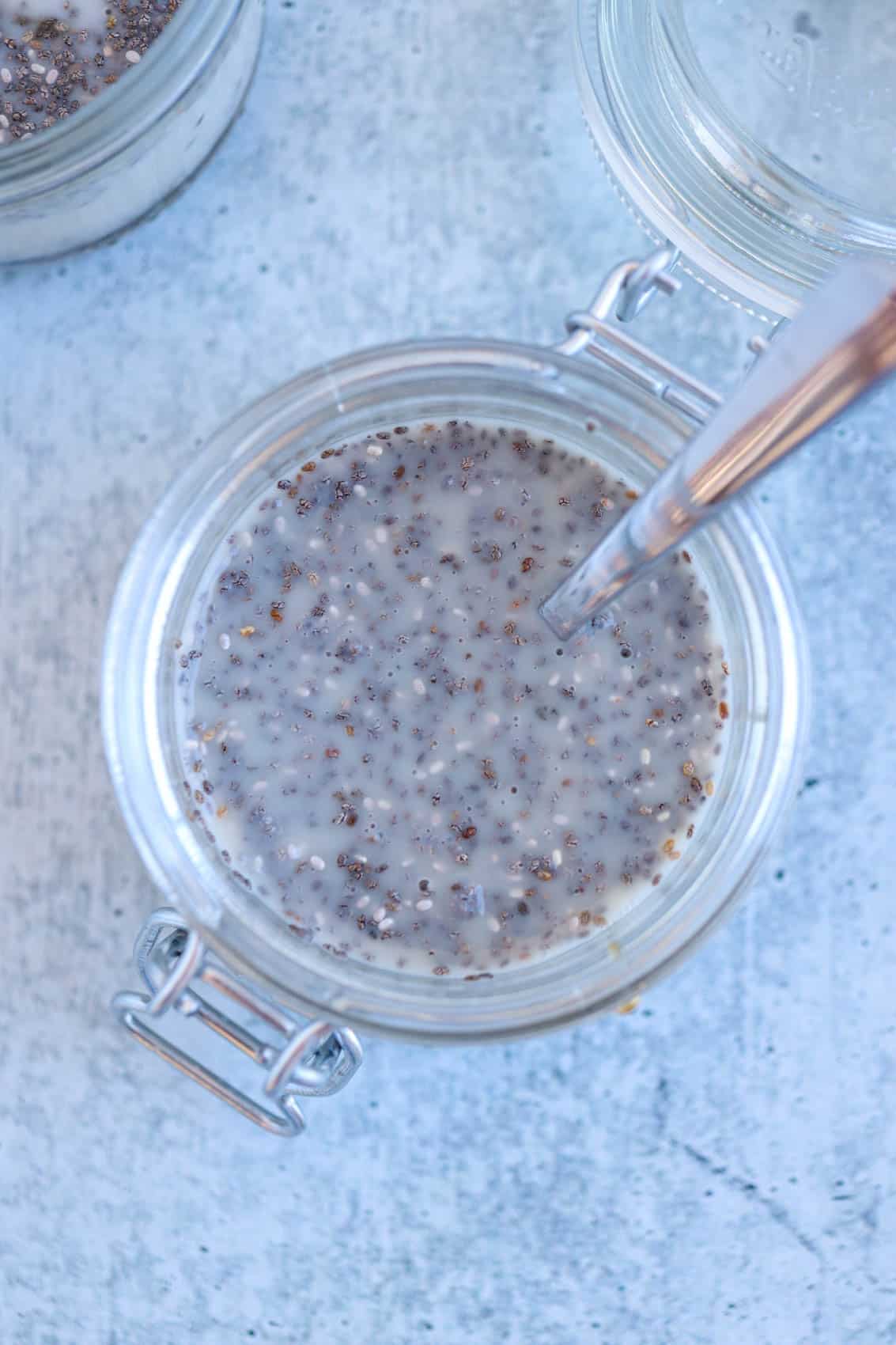 chia seed pudding in a glass jar with a spoon on gray surface.