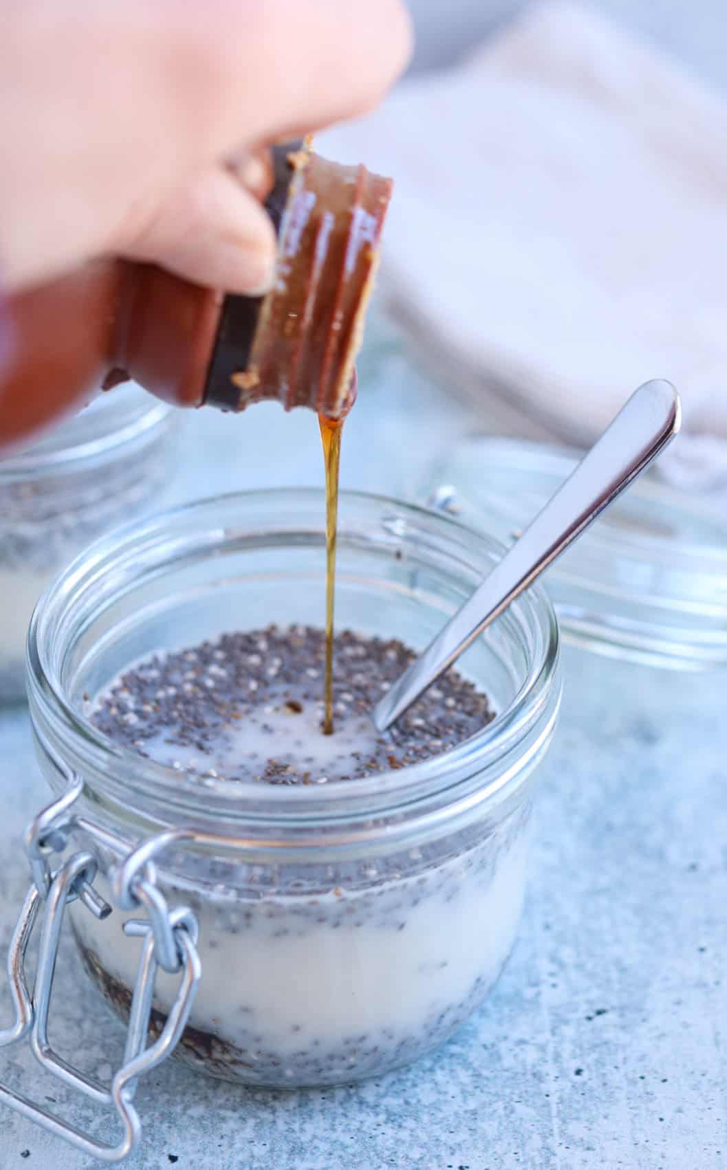 adding maple syrup to chia seed pudding in a glass jar.