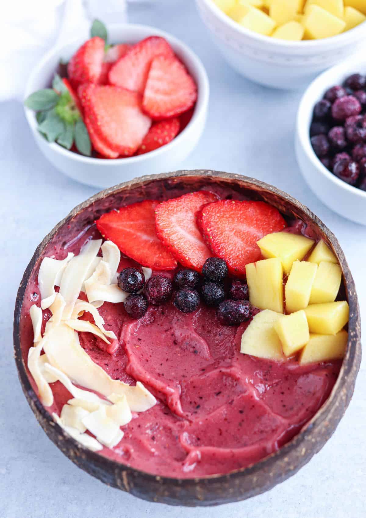 thick smoothie bowl made with frozen berries and mangoes topped with chopped mangoes, sliced strawberries, wild blueberries and coconut.