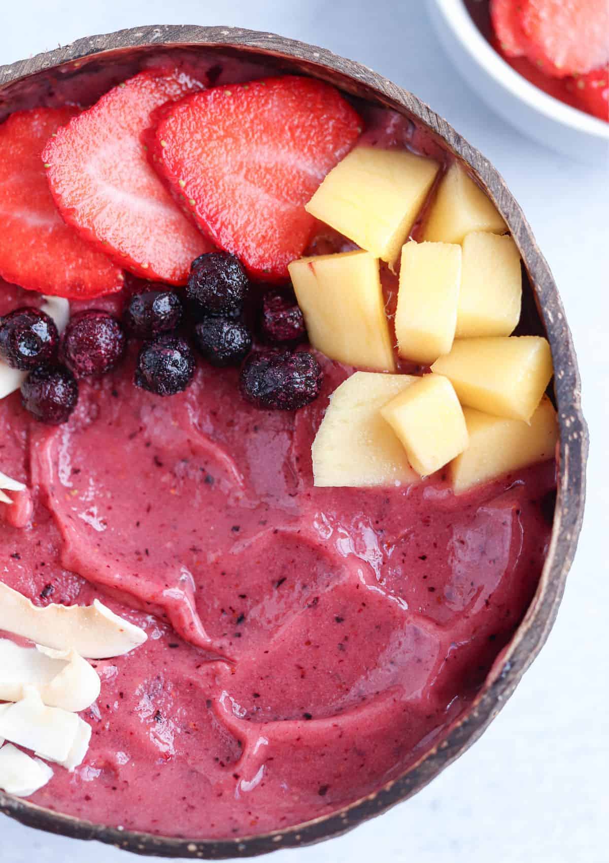 thick smoothie bowl made with frozen berries and mangoes topped with chopped mangoes, sliced strawberries, wild blueberries and coconut.