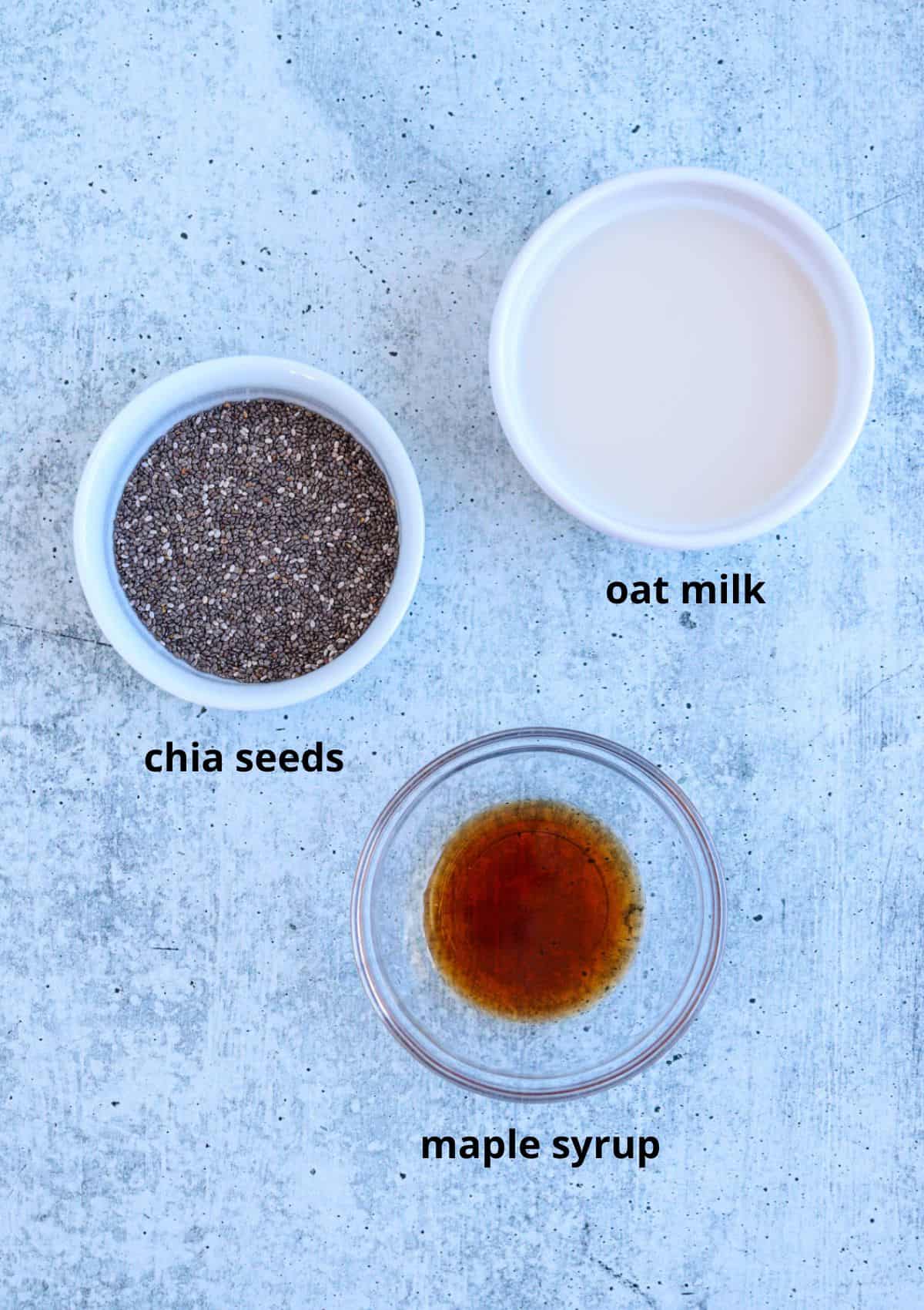 chia seeds, oat milk and maple syrup in small round containers on gray surface.