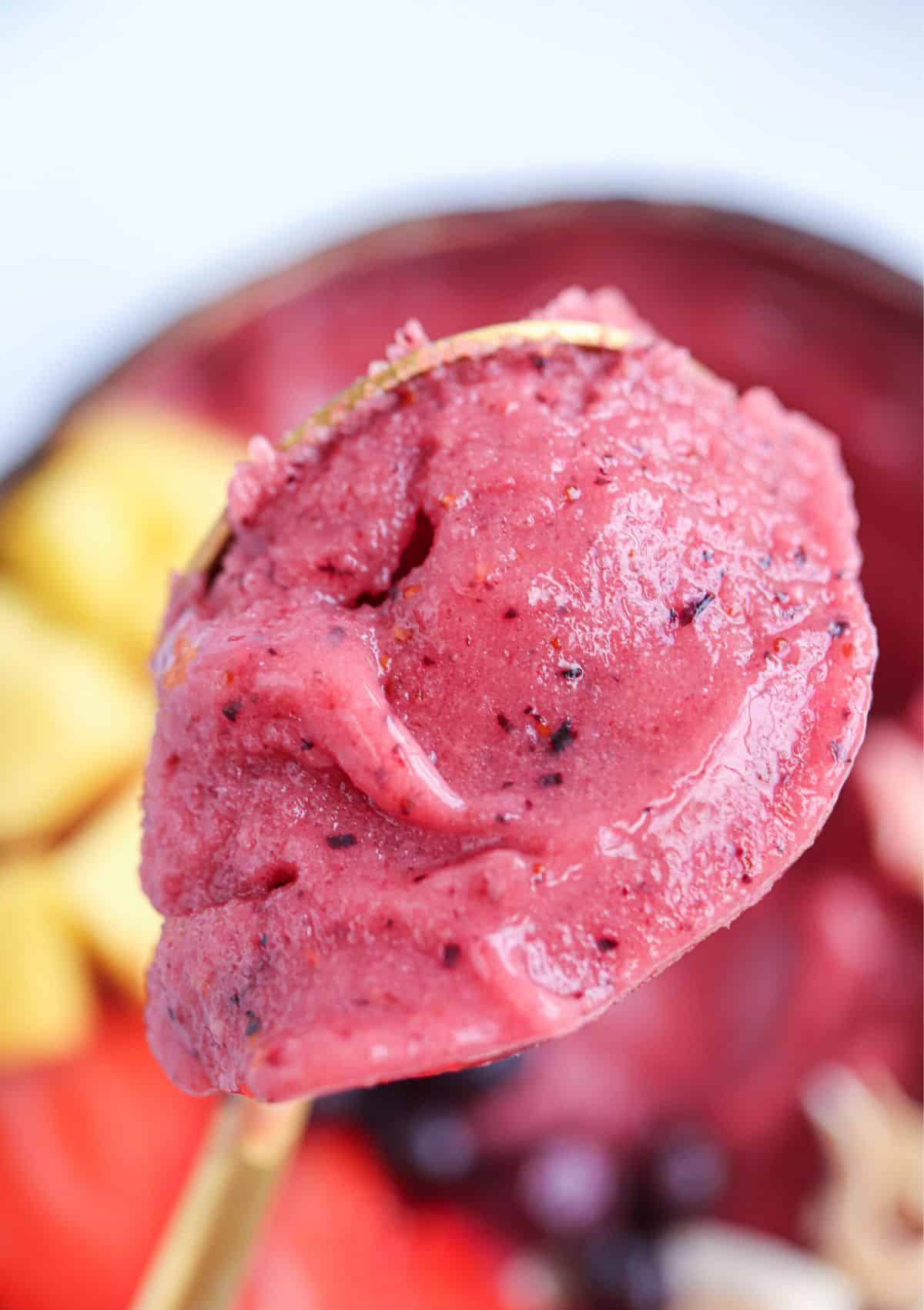 thick smoothie bowl made with frozen berries and mangoes, bite shot on a spoon.