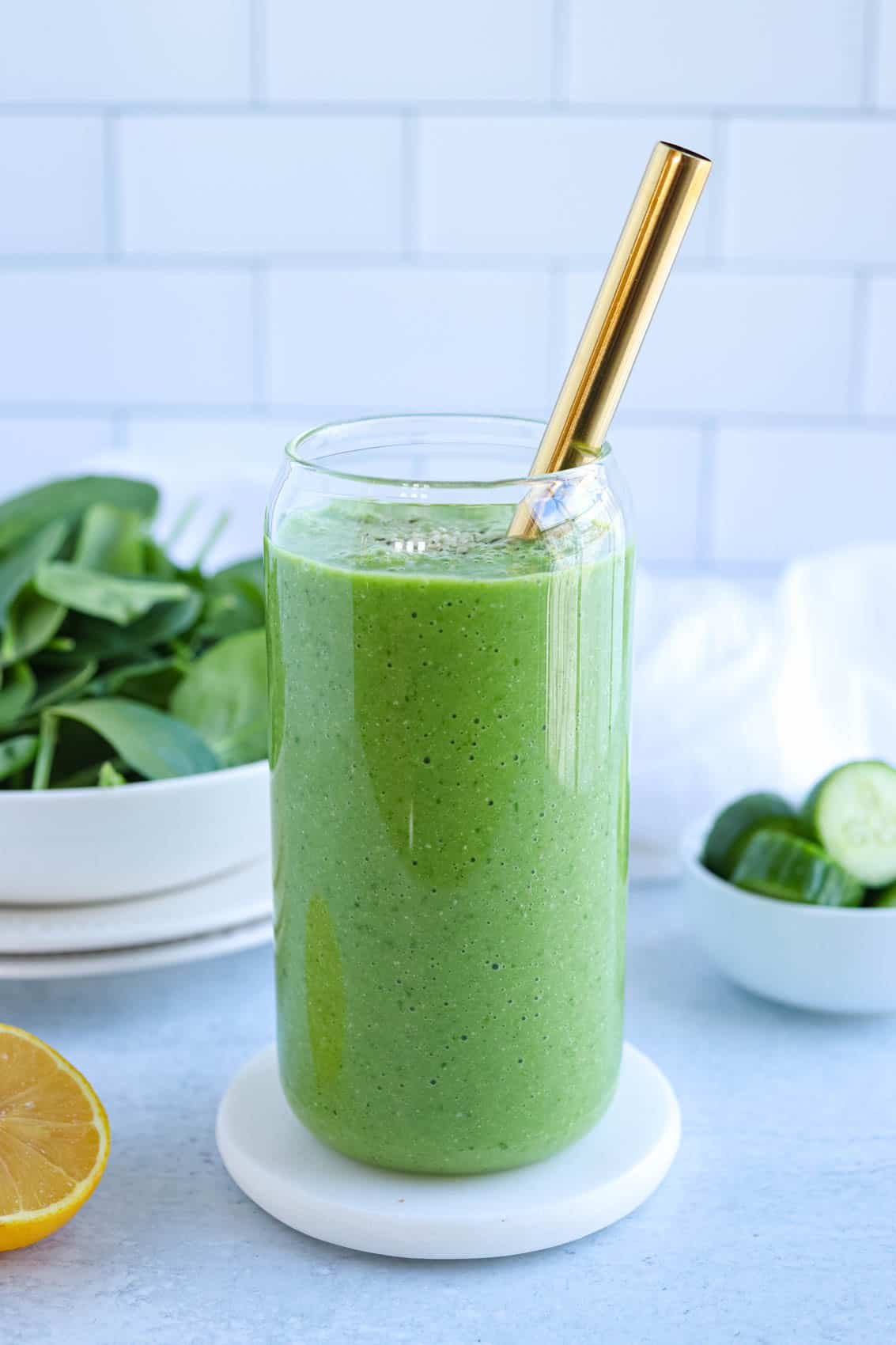 bright green spinach cucumber smoothie in a tall glass with a golden wide straw. 