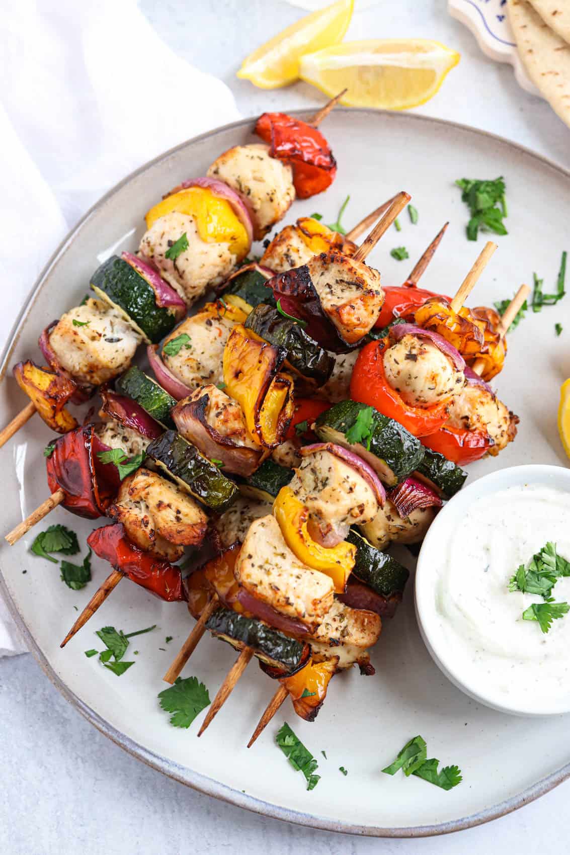 chicken and vegetable kebabs on wooden skewers stacked on a gray plate with a side of ranch dip.