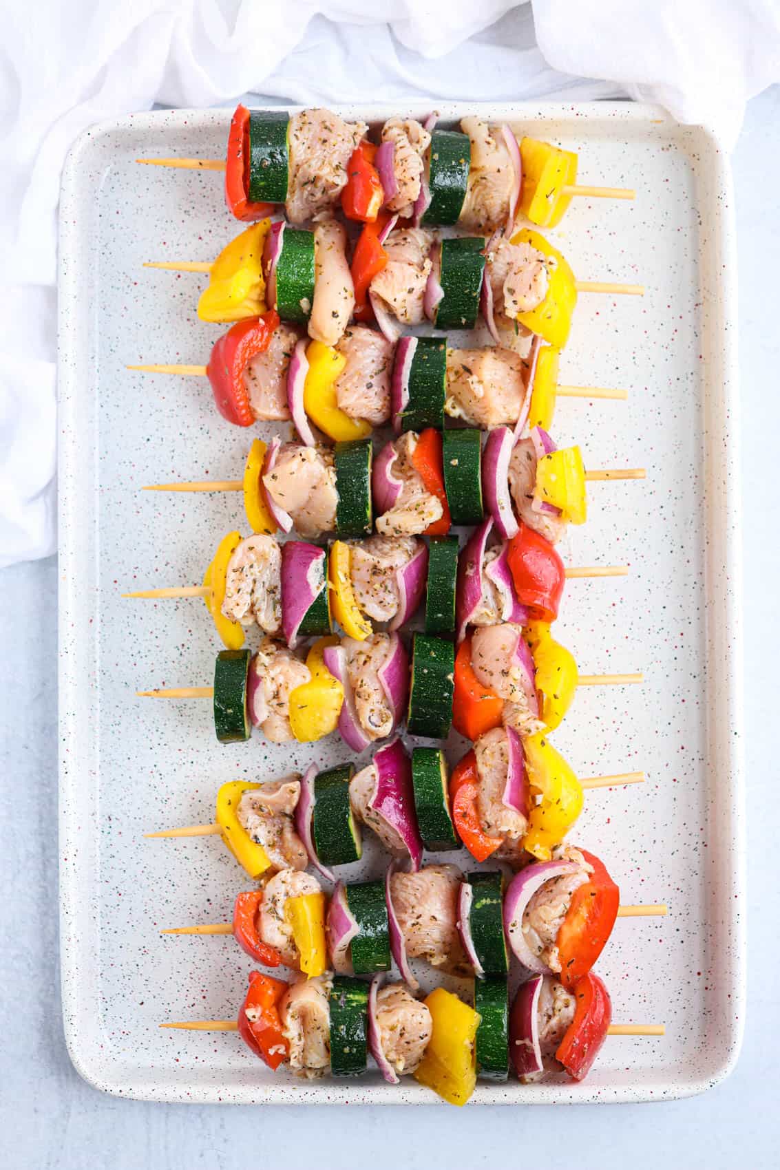 raw chicken and vegetable kebabs on wooden skewers on a baking sheet.
