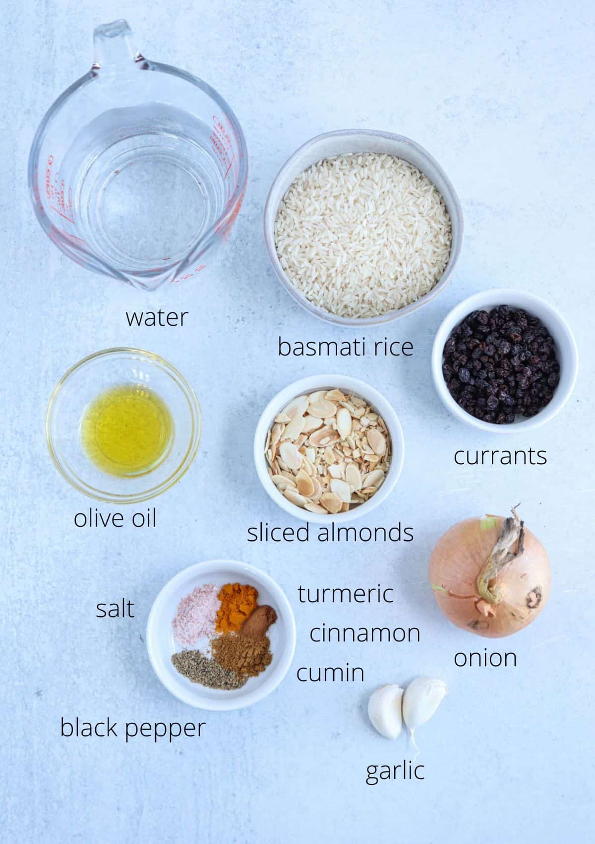 ingredients for making mediterranean yellow rice in round containers on gray surface with captions.