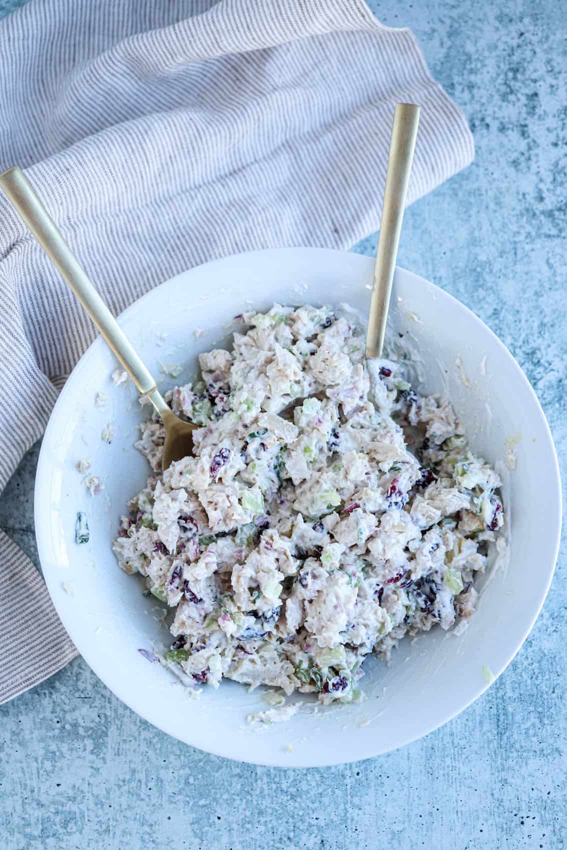 Mixing creamy chicken salad in a white bowl with two spoons.