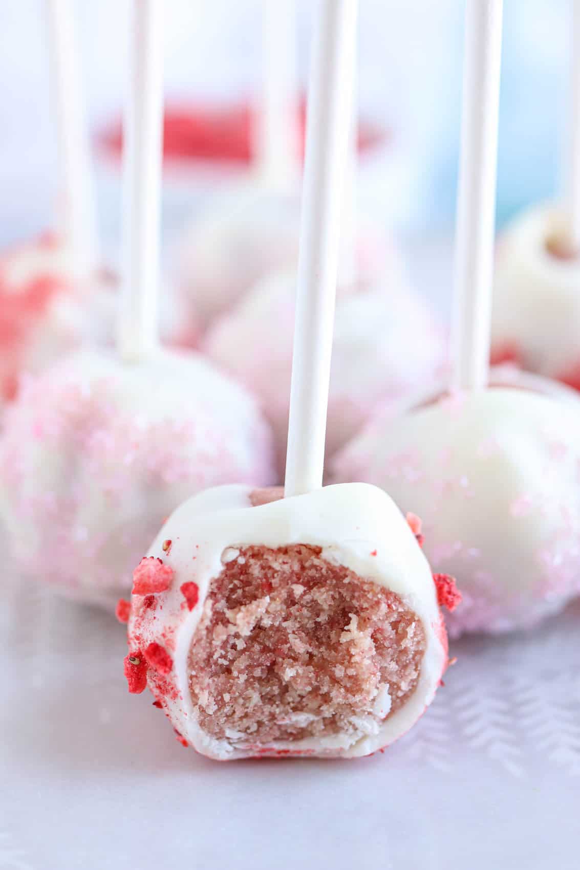 strawberry cake pops in w hite chocolate with a bite taken out.