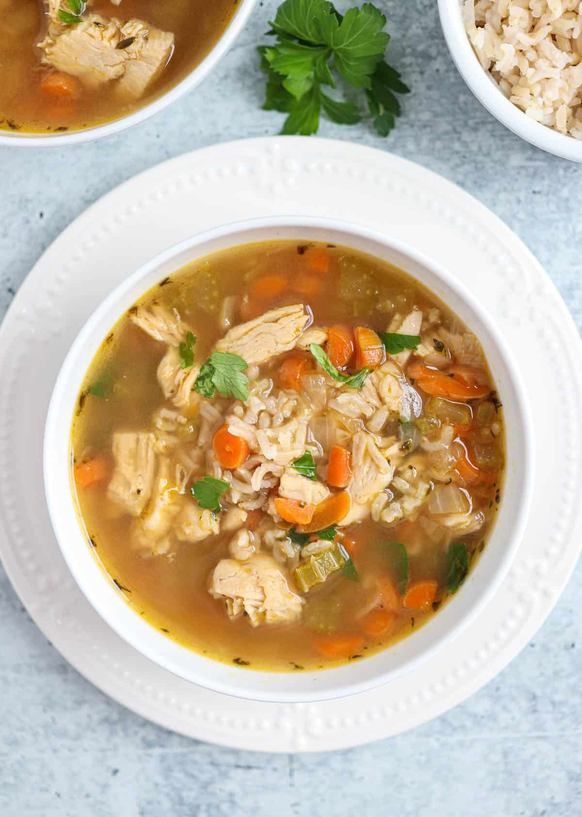 bone broth chicken soup with carrots and brown rice in a white bowl on a white plate.