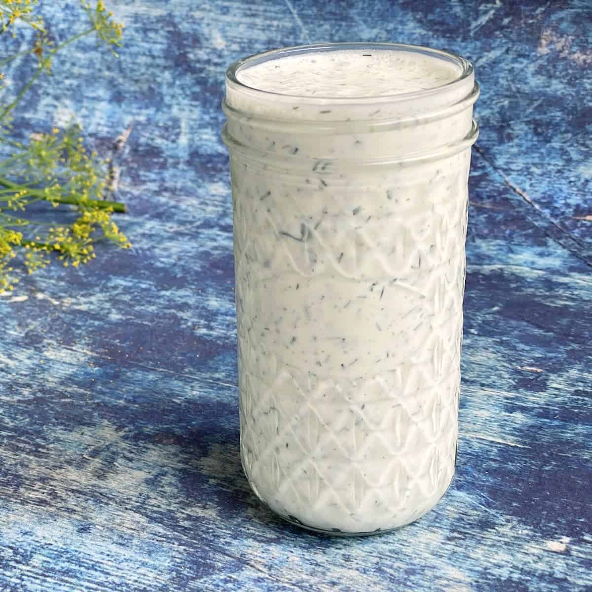 creamy sauce with herbs in a tall jar on wood background painted in blue.